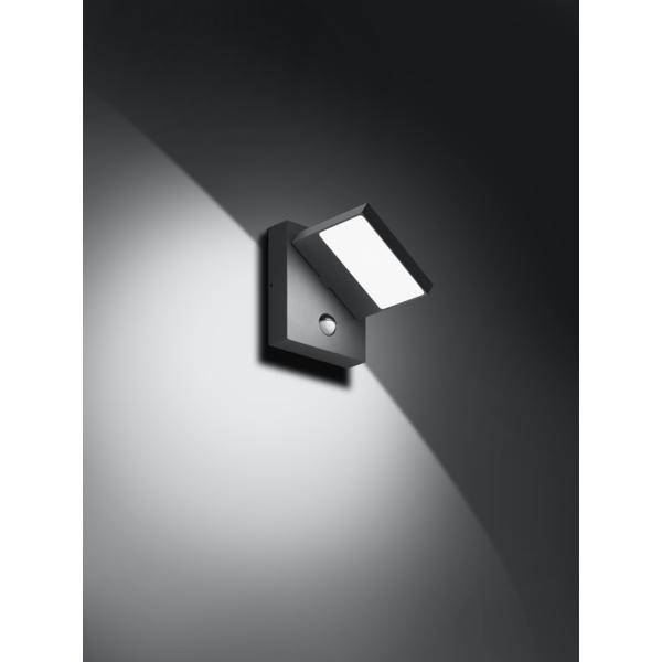 Nowoczesna, prostokątna lampa zewnętrzna zamontowana na ścianie, skierowana w dół. Tworzy ona jasny stożek światła na ciemnej powierzchni.