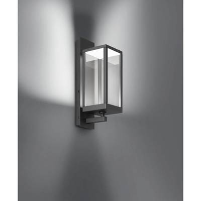 Nowoczesna lampa ścienna wykonana z metalu i szkła, rzuca białe światło na szarą ścianę, tworząc stylową atmosferę.