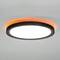 Okrągła lampa sufitowa z białą, świecącą powierzchnią i pomarańczowym pierścieniem świetlnym, zamocowana na szarym suficie.