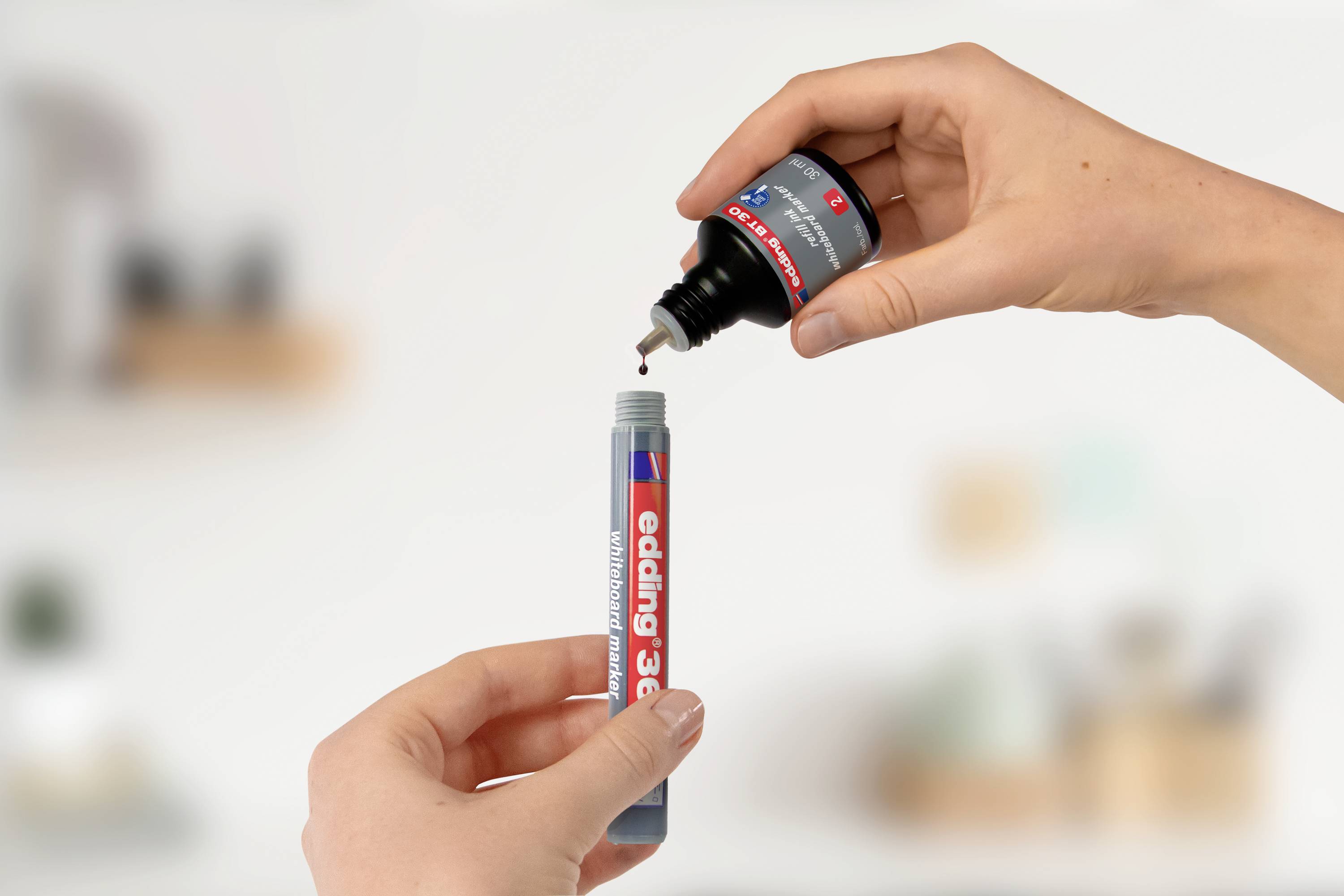 Dwie dłonie podczas napełniania markera edding 3000 tuszem. Jedna dłoń trzyma marker, druga dodaje tusz.