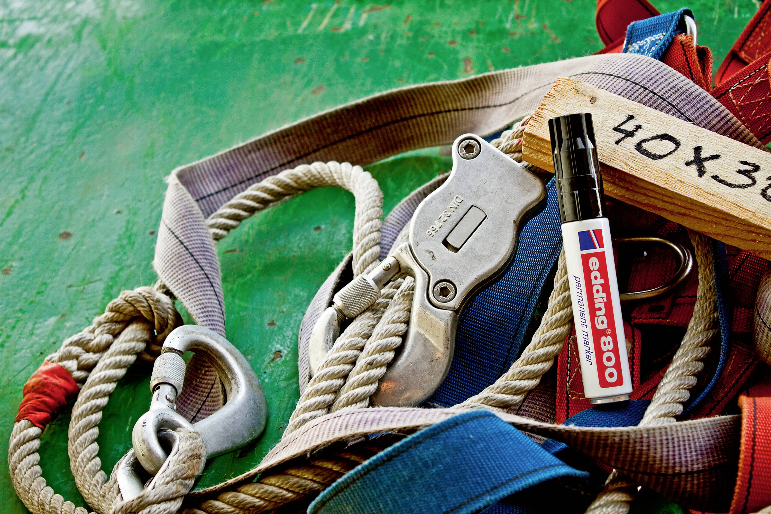 Sprzęt alpinistyczny: lina, karabińczyk, uprząż wspinaczkowa i marker Edding 800 leżą obok siebie na zielonym podłożu.
