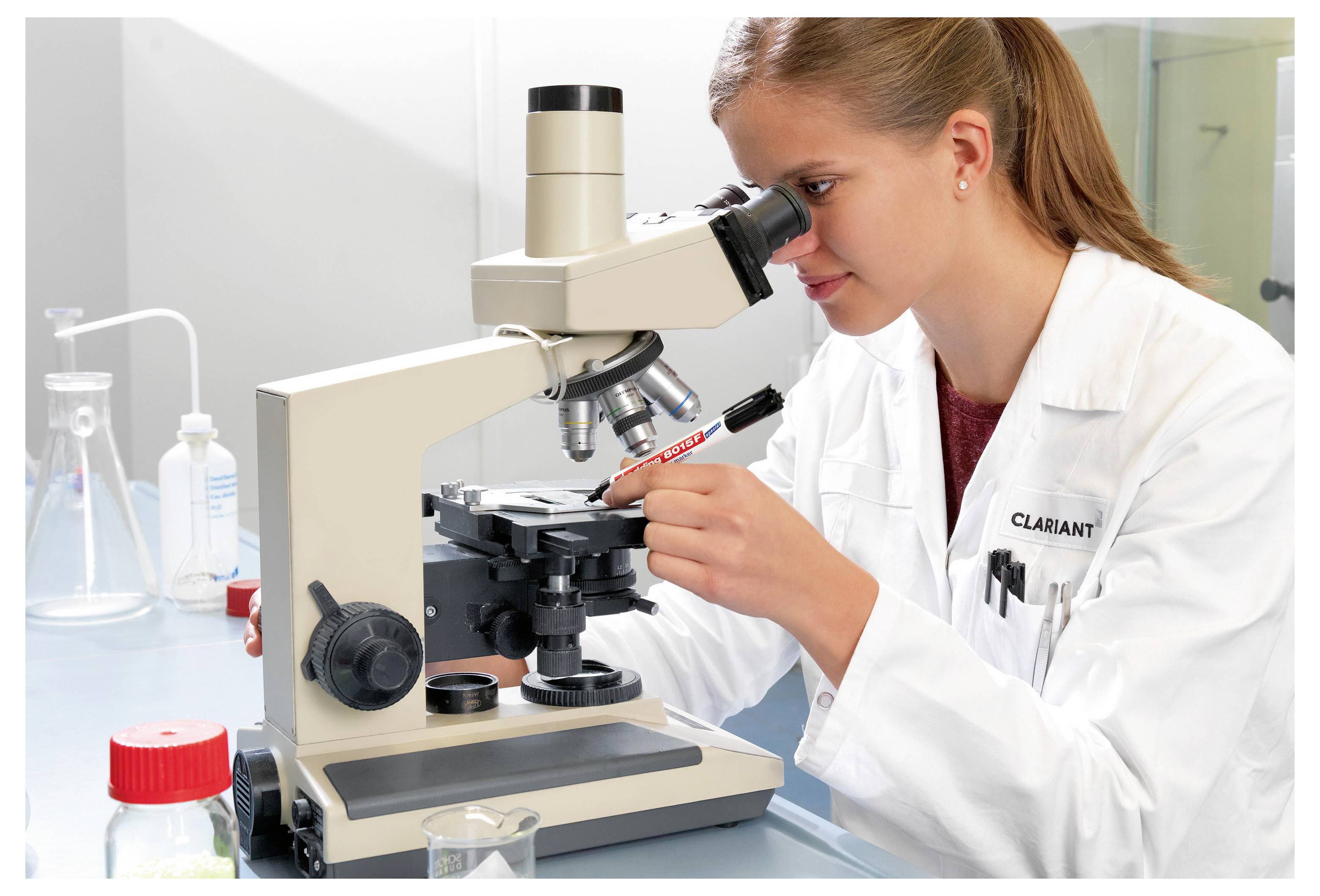 Naukowiec w białym fartuchu badający próbkę pod mikroskopem w laboratorium.