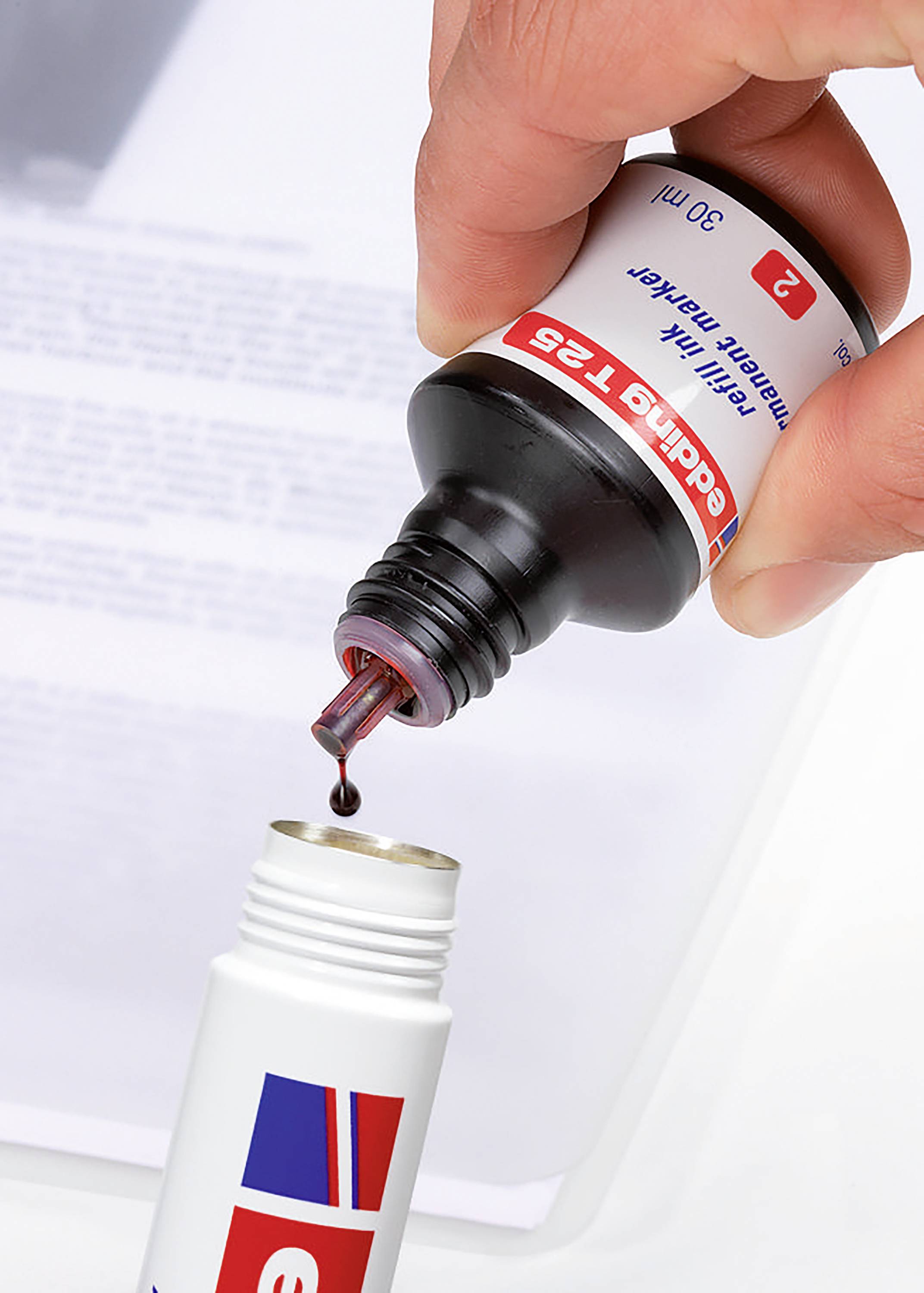 Dłoń napełnia małą buteleczkę czerwonym płynem z butelki z zakraplaczem. W tle widać rozmyty dokument.