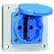 Niebieskie gniazdo elektryczne z bolcem ochronnym i klapką zamontowane na białej płycie.