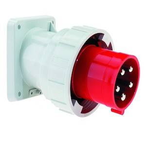 Przemysłowe gniazdo elektryczne z czerwoną wtyczką i wieloma stykami metalowymi, zamontowane na białej płytce ściennej.