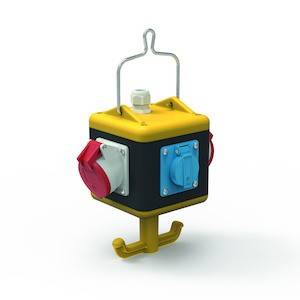 Żółta kostka z gniazdkami elektrycznymi i hakiem na górze. Po bokach znajdują się czerwone i niebieskie złącza.