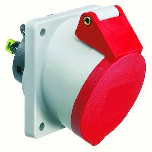 Czerwona i biała przemysłowa wtyczka na uchwycie ściennym. Posiada mechanizm obrotowy zabezpieczający połączenie.