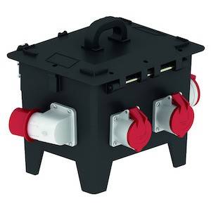 Przenośna rozdzielnica elektryczna z wieloma czerwonymi i białymi przyłączami na czarnej obudowie, przeznaczona do użytku na placach budów.