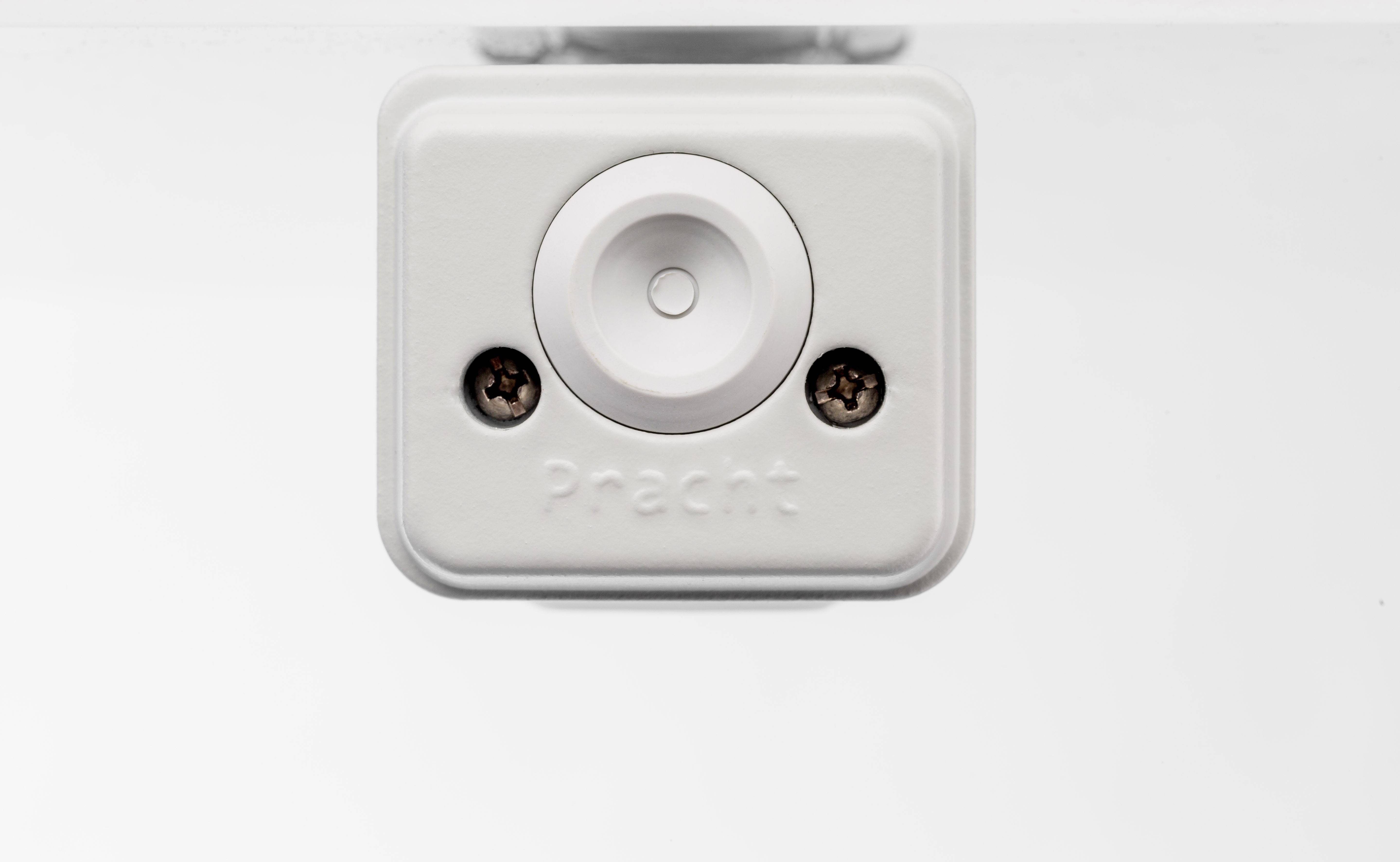 Biała plastikowa skrzynka z dwoma widocznymi śrubami, centralnym okrągłym przyciskiem.