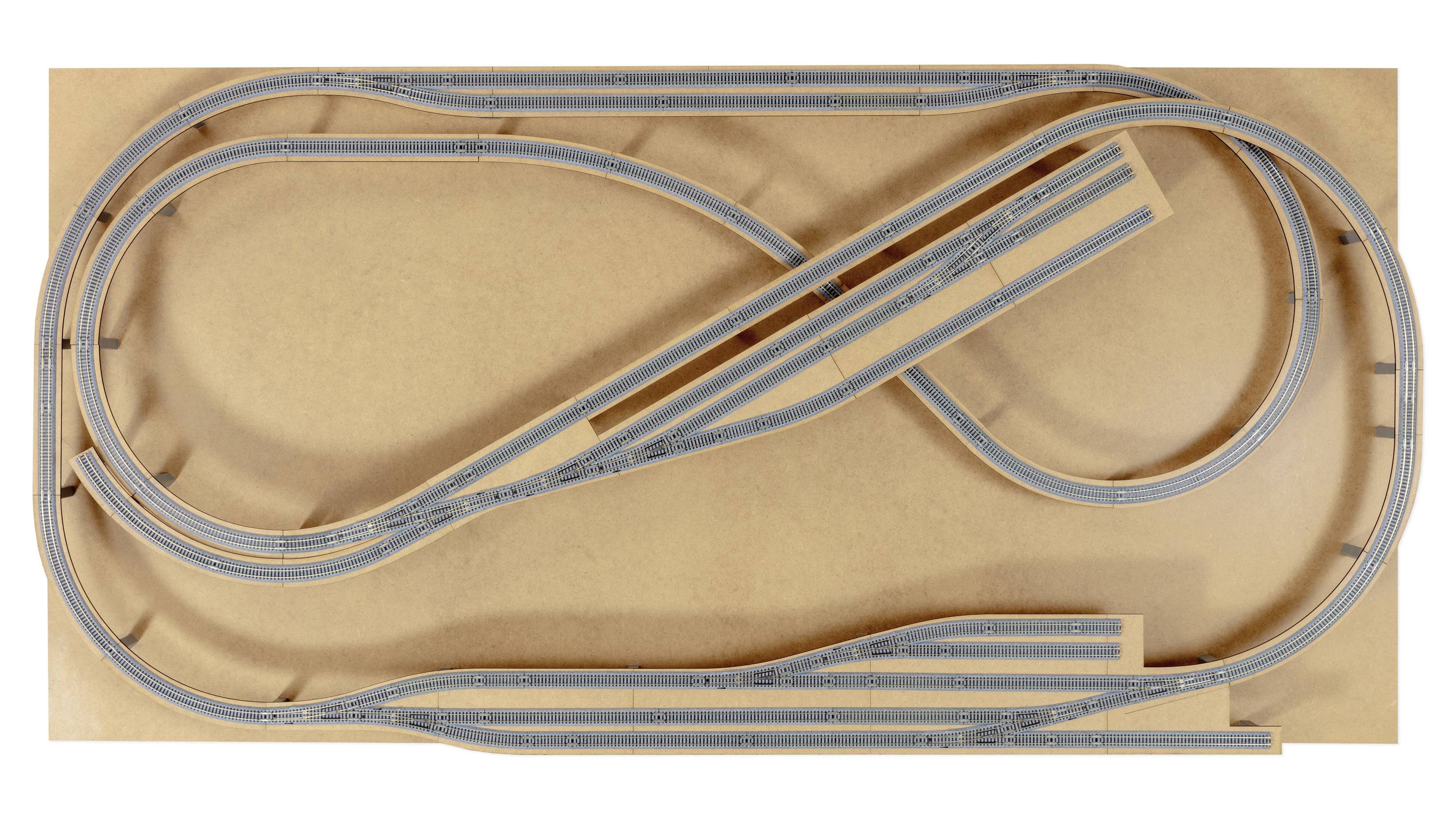 Kolejka modelowa z wieloma pętlami i zwrotnicami, zamontowana na prostokątnej drewnianej płycie. Wiązka równoległych torów w centrum.