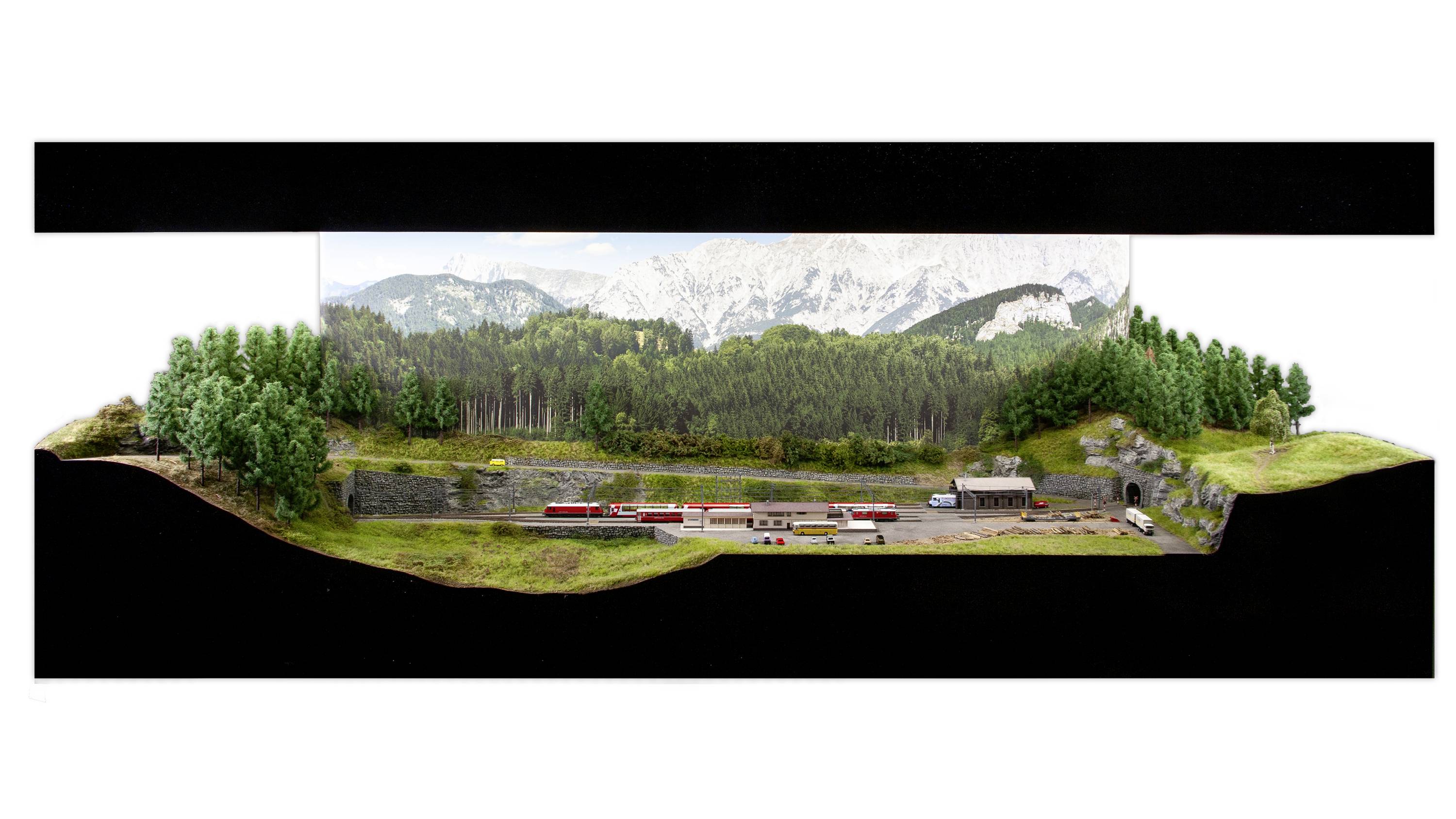 Miniaturowy model krajobrazu z pociągiem jadącym przez zalesiony region górski. Otoczony świerkami, z górami w tle.