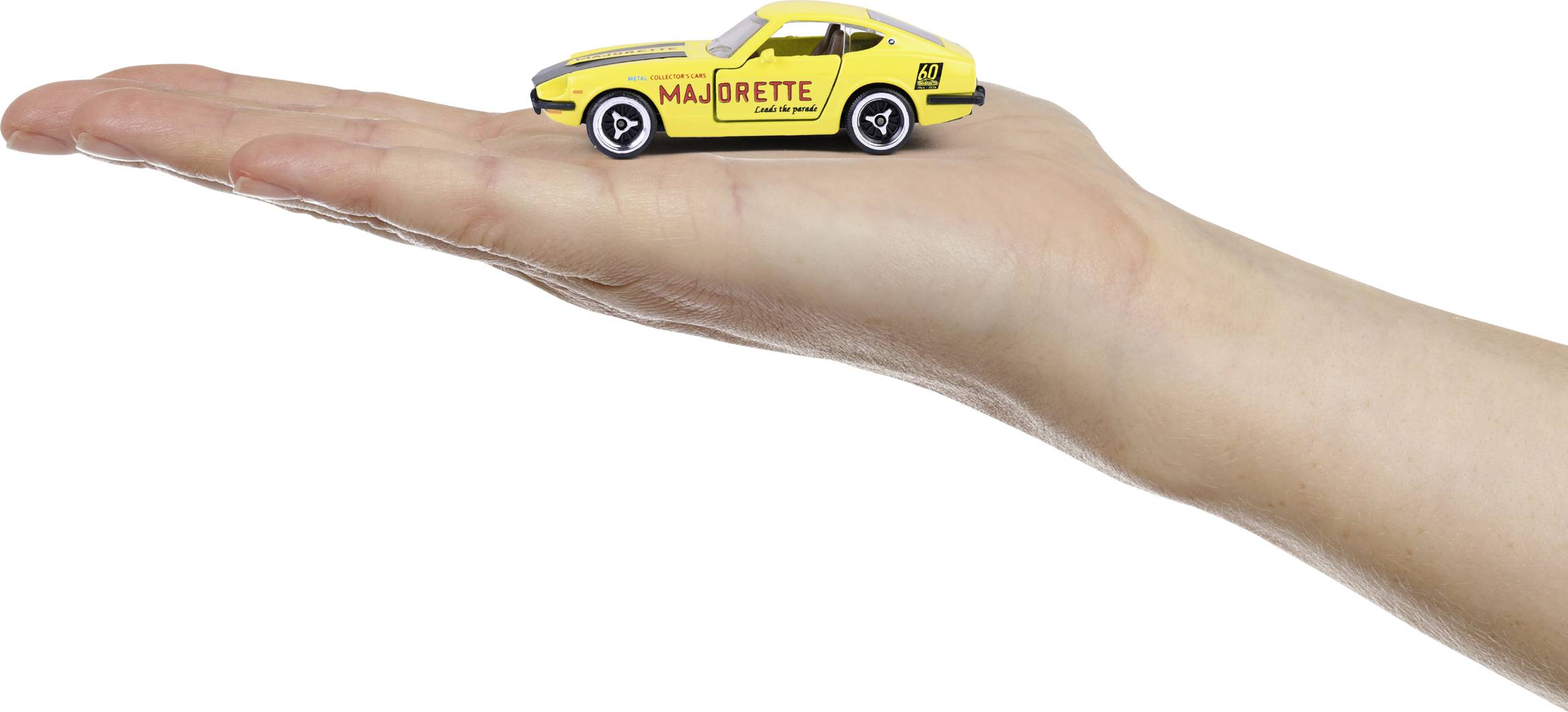 Ręka trzyma małą żółtą zabawkową ciężarówkę z napisem 'Majorette' z boku.