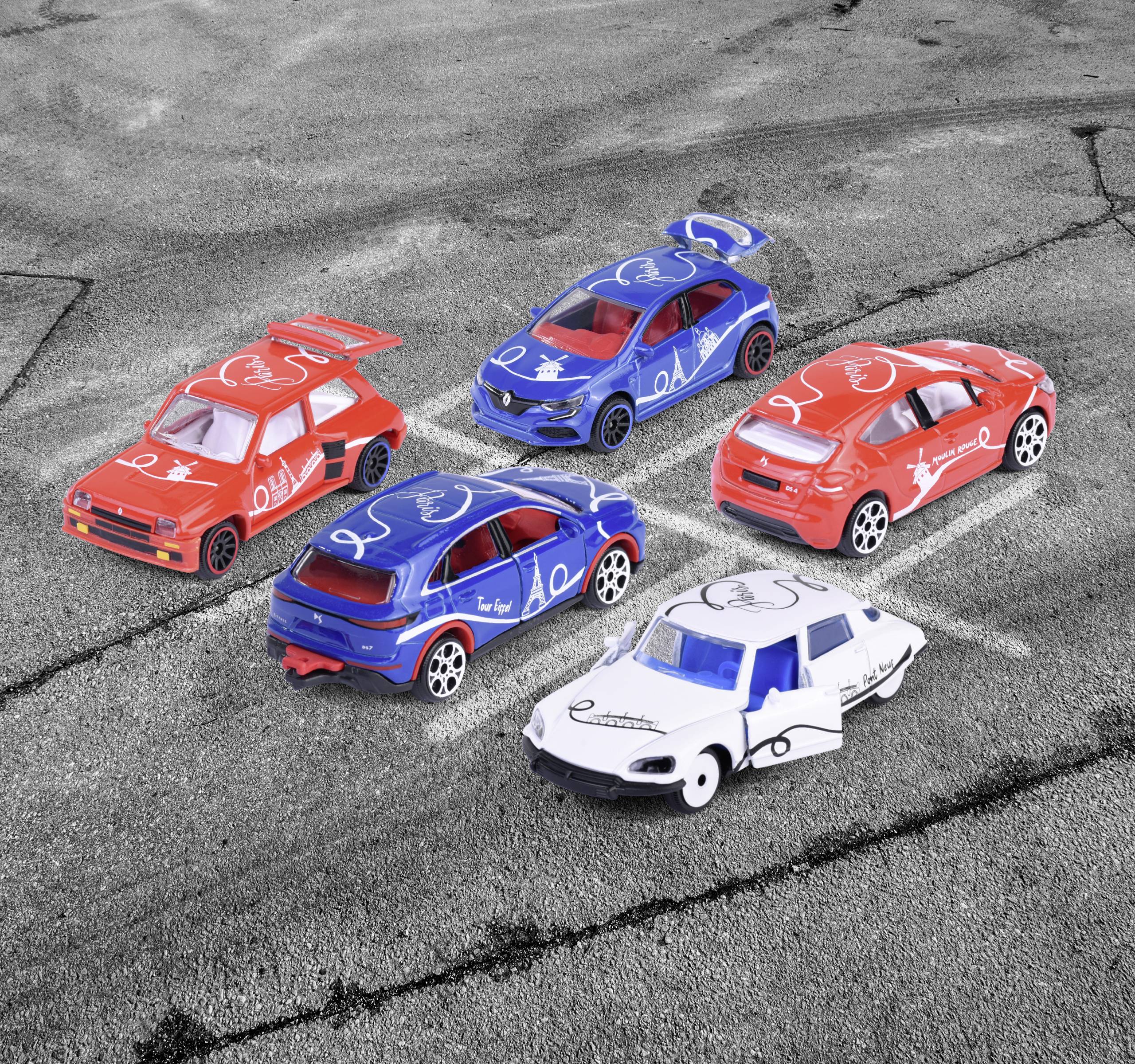 Pięć małych zabawkowych samochodów wyścigowych w kolorach czerwonym, niebieskim i białym stoi na utwardzonej powierzchni. Są kolorowo pomalowane i ponumerowane.