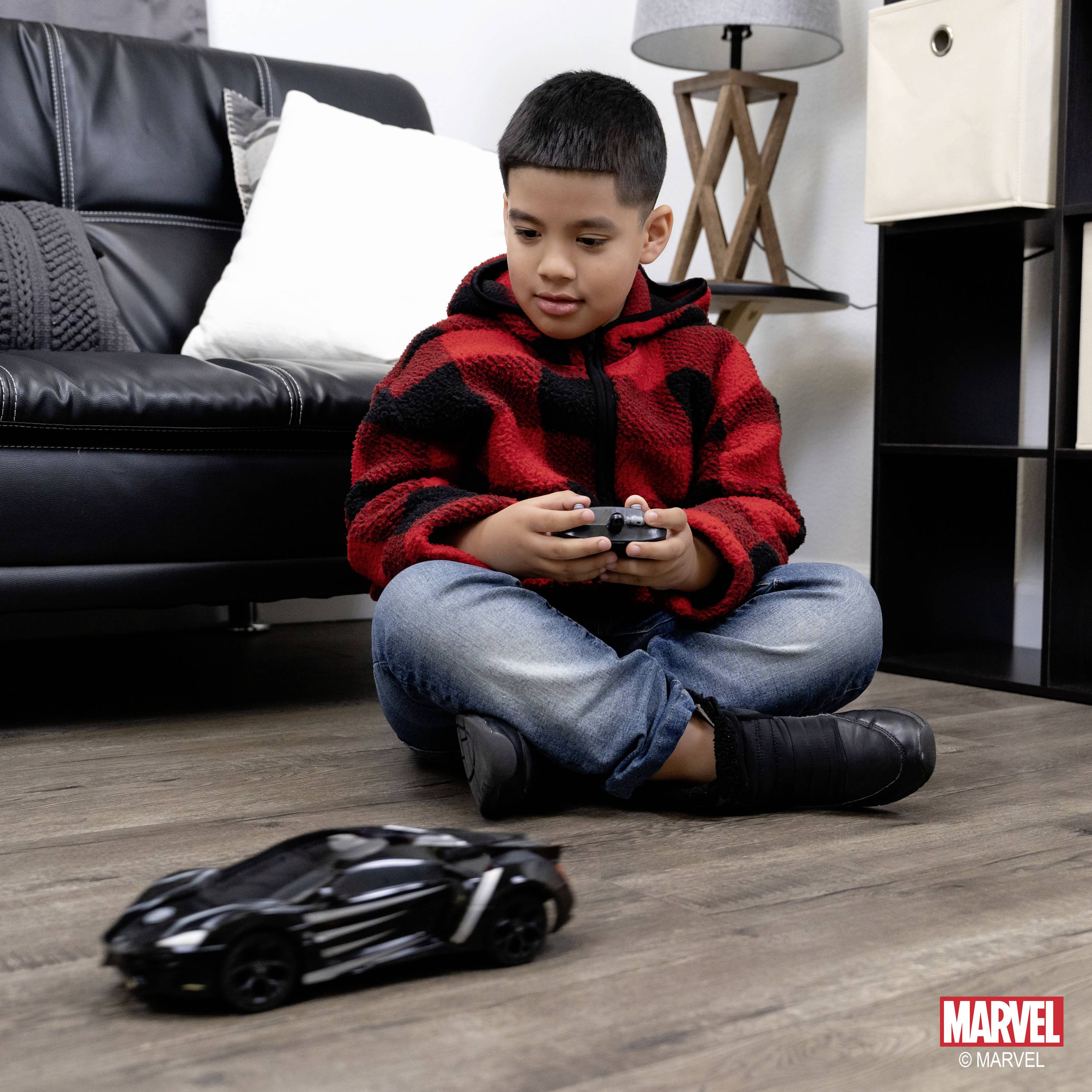 Chłopiec siedzi na podłodze i steruje małym, czarnym samochodzikiem za pomocą kontrolera. W tle widać kanapę.