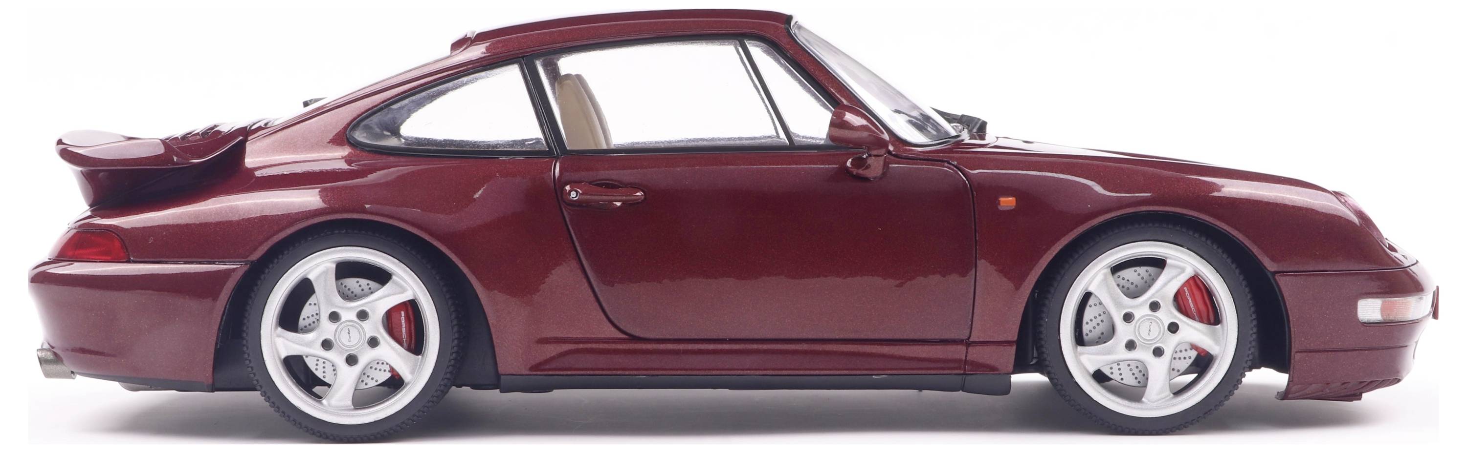 Czerwony model samochodu sportowego widziany z profilu, z białymi felgami i czerwonym zaciskiem hamulcowym, na białym tle.