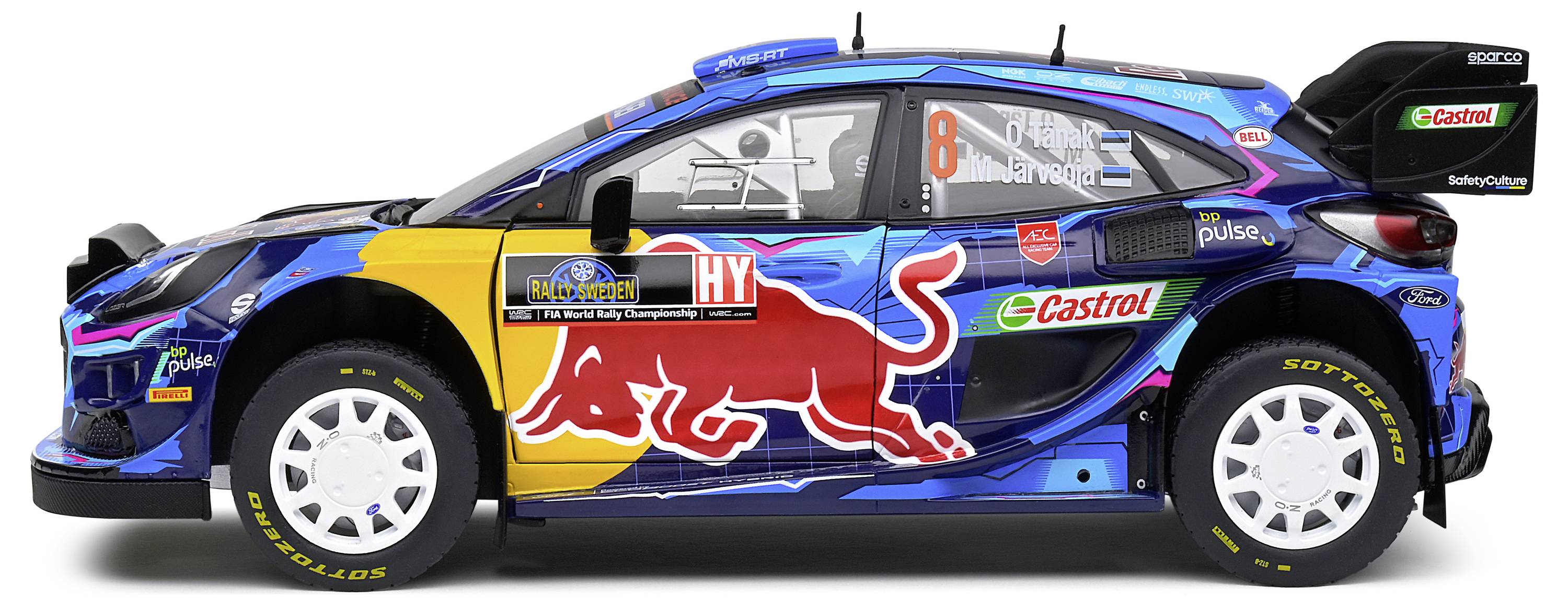 Samochód rajdowy z kolorowym, sponsorowanym malowaniem, w tym widoczne, rzucające się w oczy czerwone logo byka. Pojazd ma numer 8.