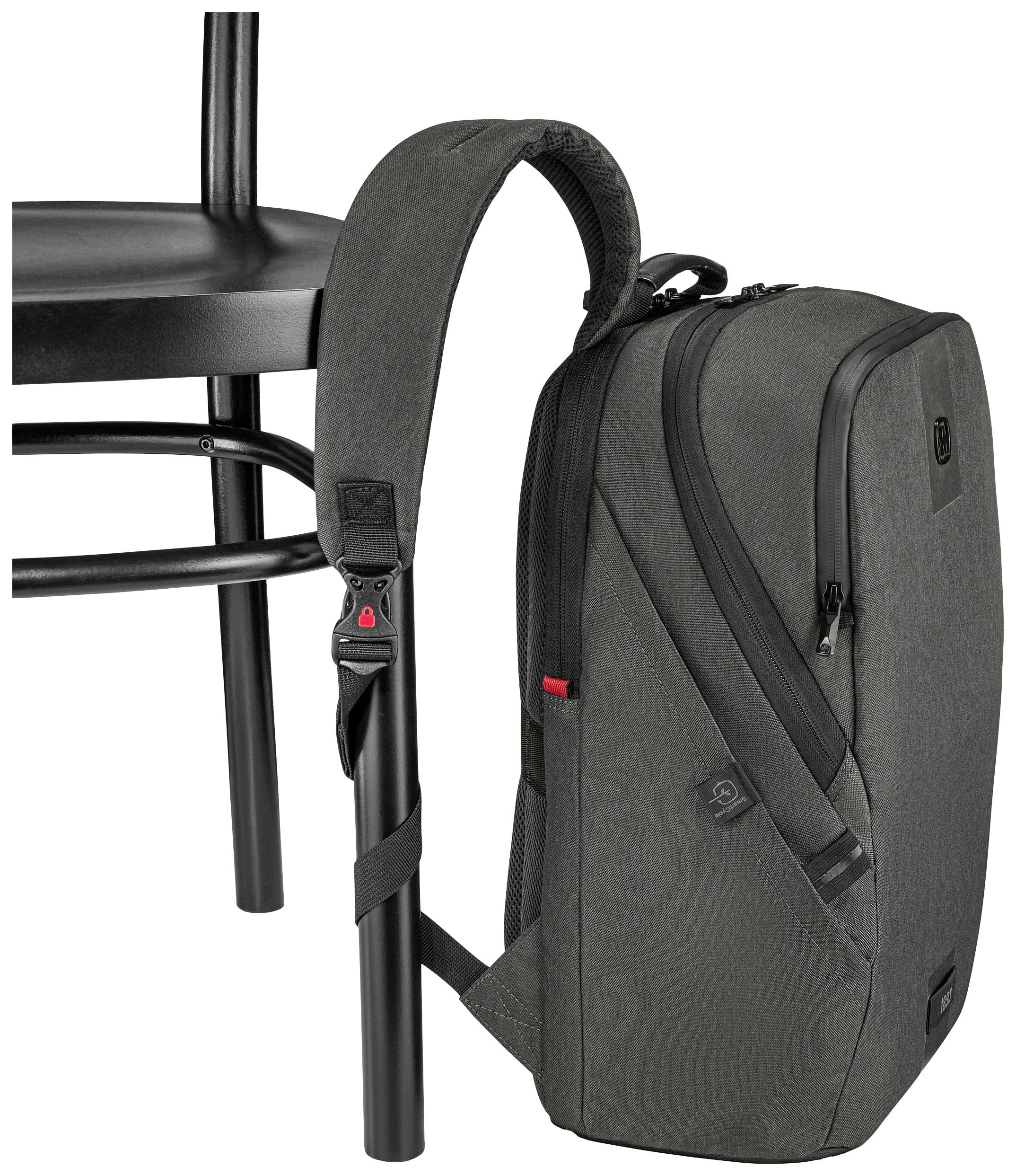 Szary plecak wisi na czarnym krześle, przymocowany paskiem. Plecak posiada kilka kieszeni i zamek błyskawiczny.