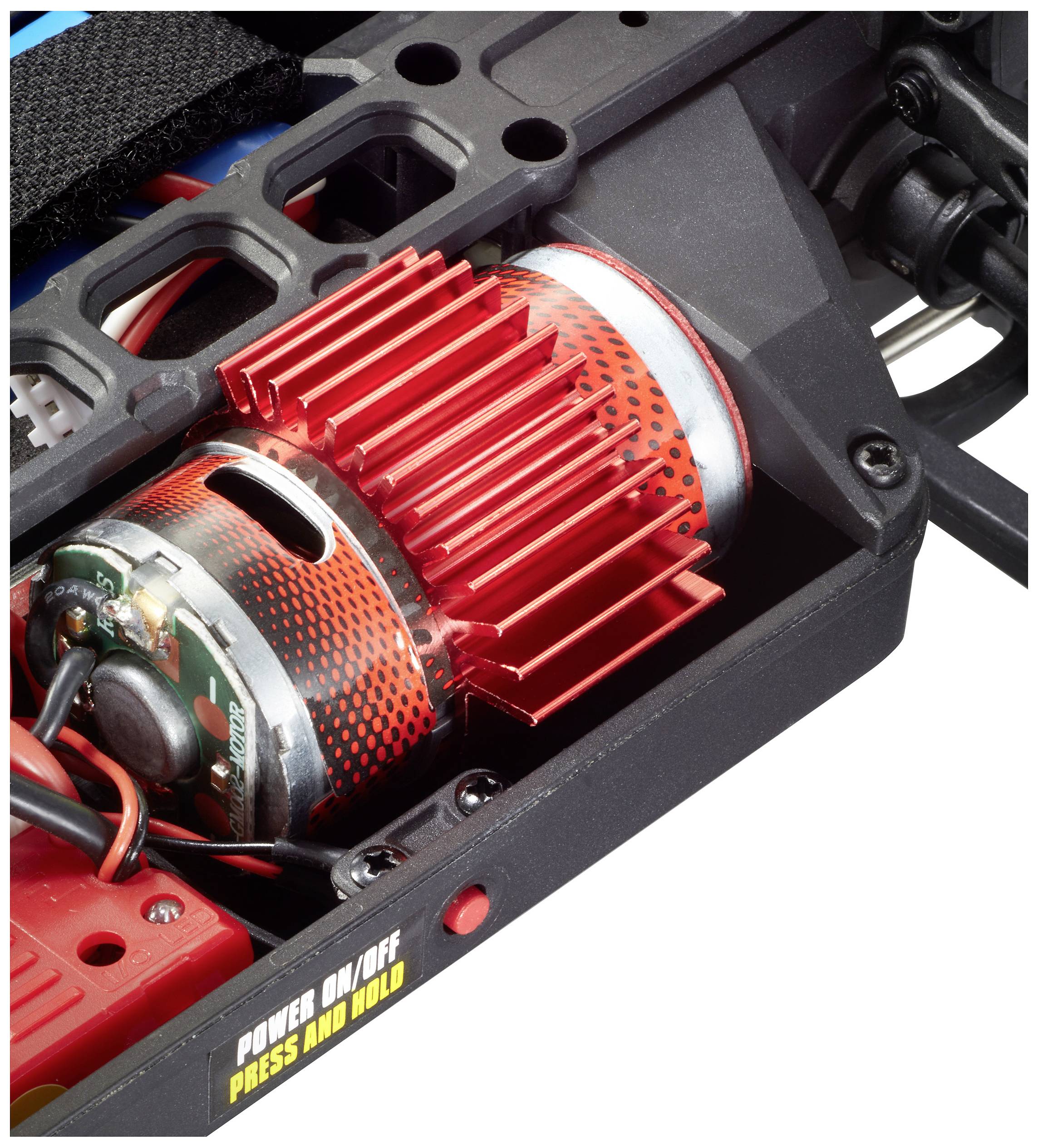 Zbliżenie czerwonego silnika elektrycznego z żebrami chłodzącymi w urządzeniu technicznym. Żółty przełącznik z napisem 'WŁĄCZ/WYŁĄCZ NACIŚNIJ I PRZYTRZYMAJ'.