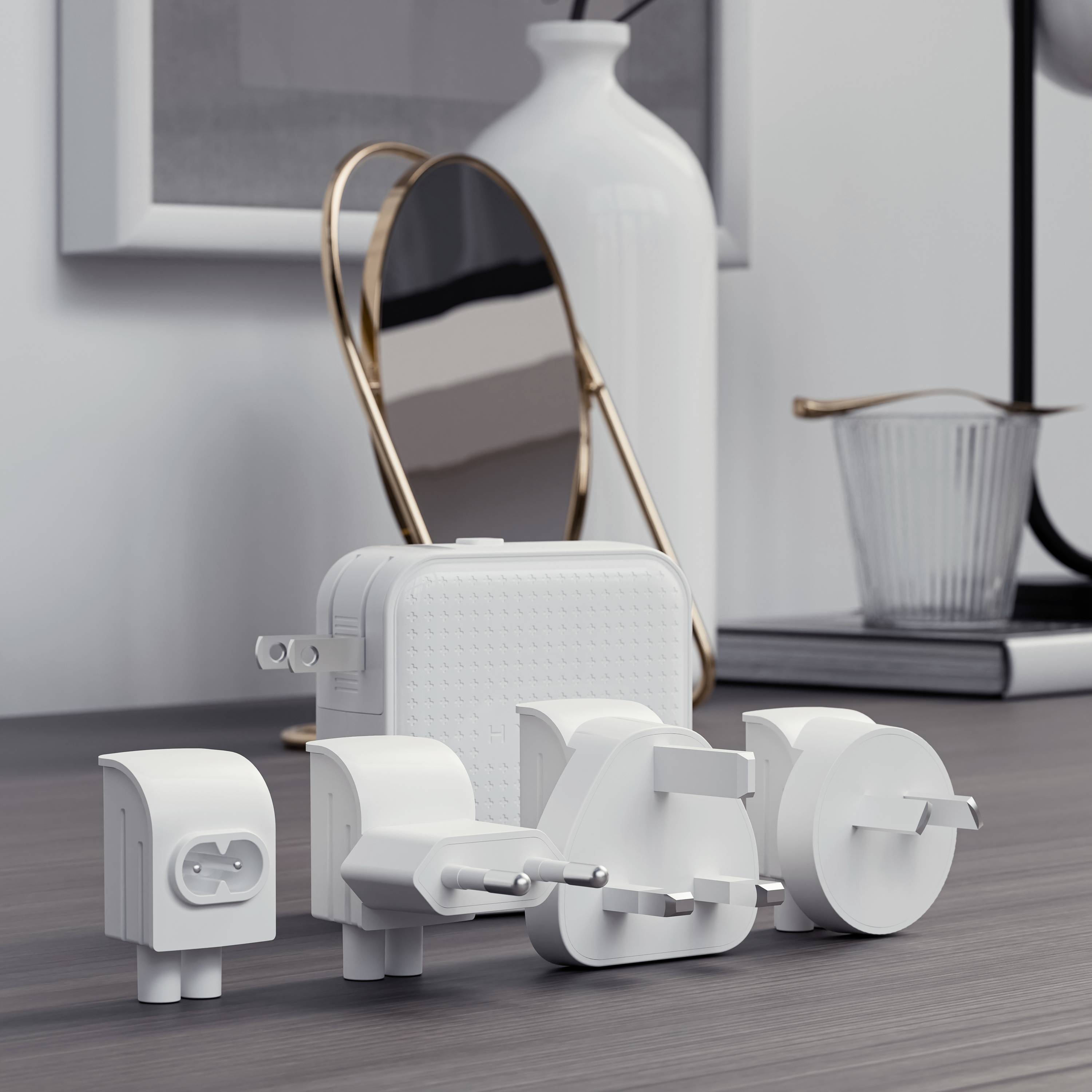 Kilka międzynarodowych adapterów elektrycznych leżących na stole, z wazonem, lustrem i książką w tle.