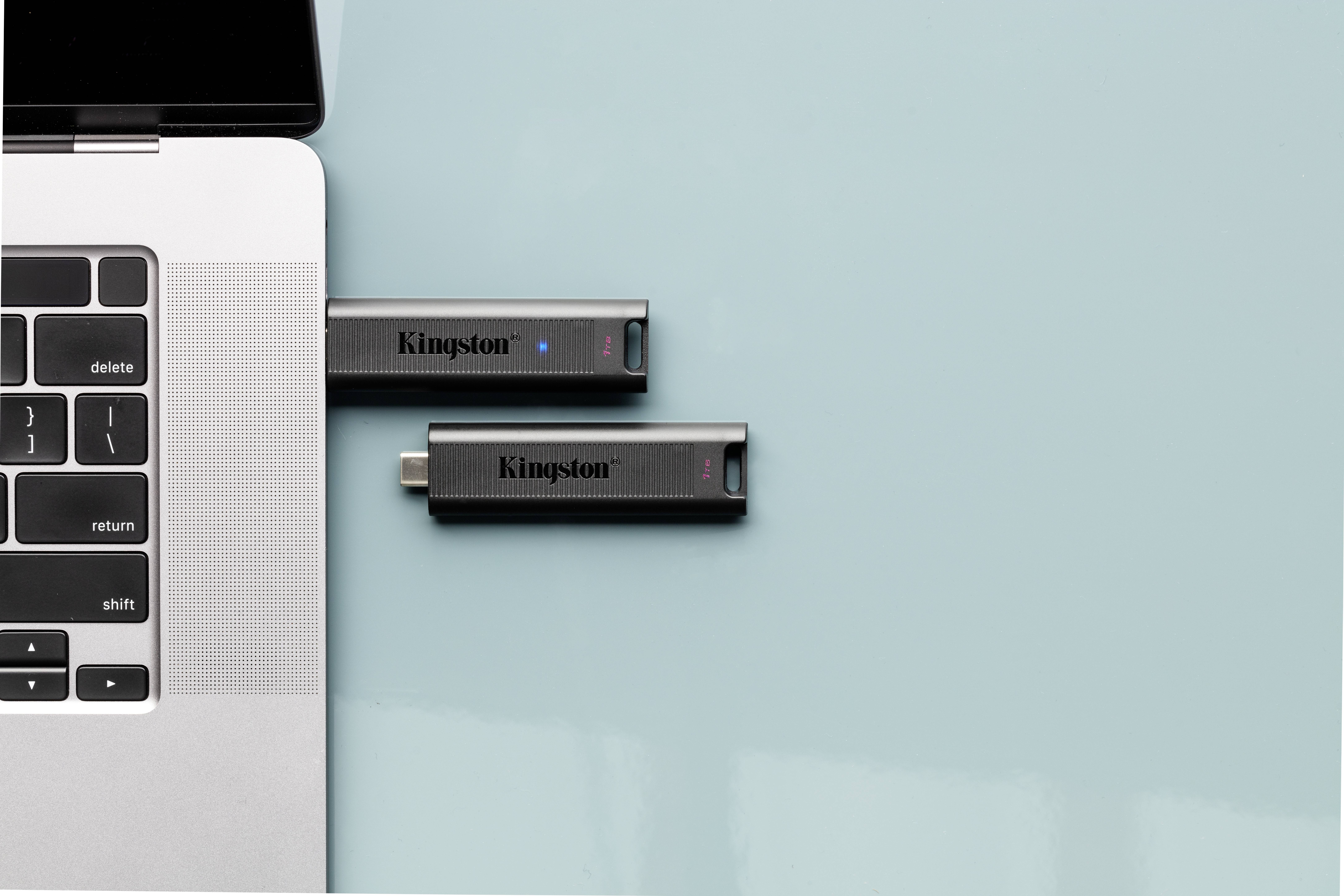 Laptop z czarną klawiaturą ma włożone dwa pendrive'y firmy Kingston. Jeden jest podłączony do laptopa, drugi leży obok.