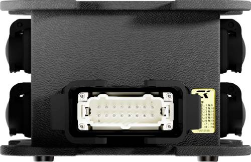 Czarne urządzenie elektryczne z wielostykową wtyczką pośrodku i żółtą etykietą z boku, umieszczone na metalowej powierzchni.