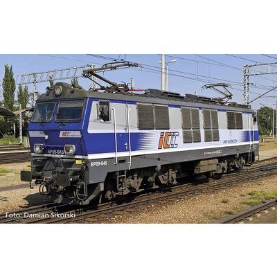 Niebieska i srebrna lokomotywa elektryczna serii EP09 stoi na torach, otoczona siecią trakcyjną i słonecznym niebem.