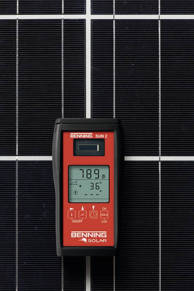Czerwone urządzenie z wyświetlaczem pokazuje '789' i '36°', oparte o powierzchnię modułu słonecznego, prawdopodobnie do pomiaru wydajności.
