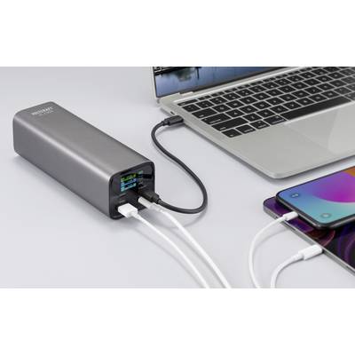 Szary powerbank ładuje jednocześnie laptopa i smartfona. Podłączonych jest kilka różnych kabli.