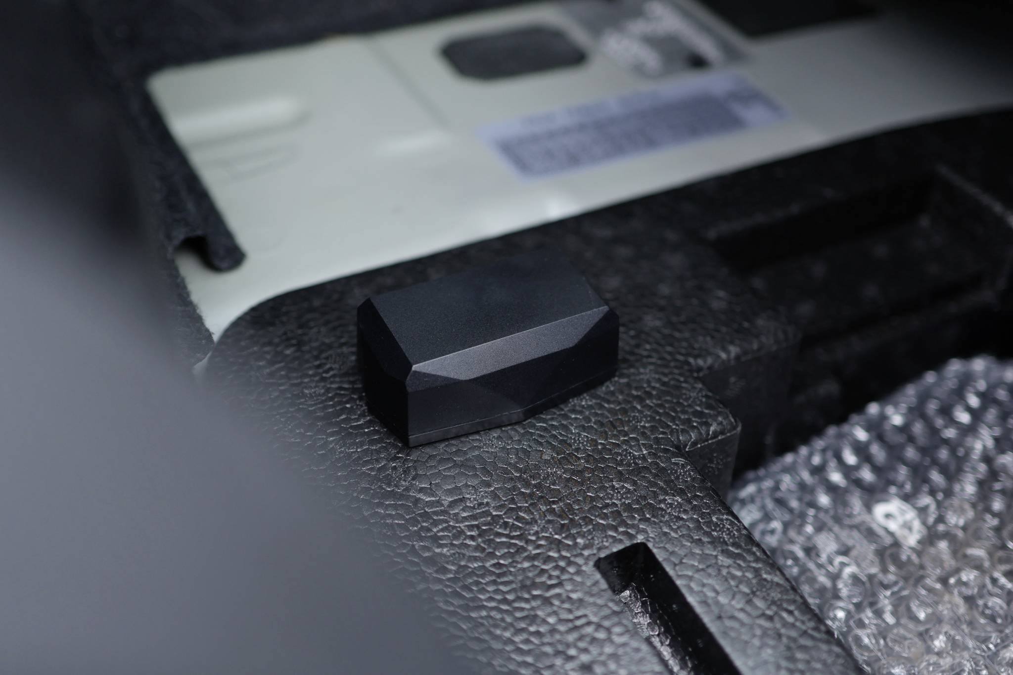 Czarny, fasetowany kamień lub obiekt leży na wyściełanym podłożu we wnętrzu.