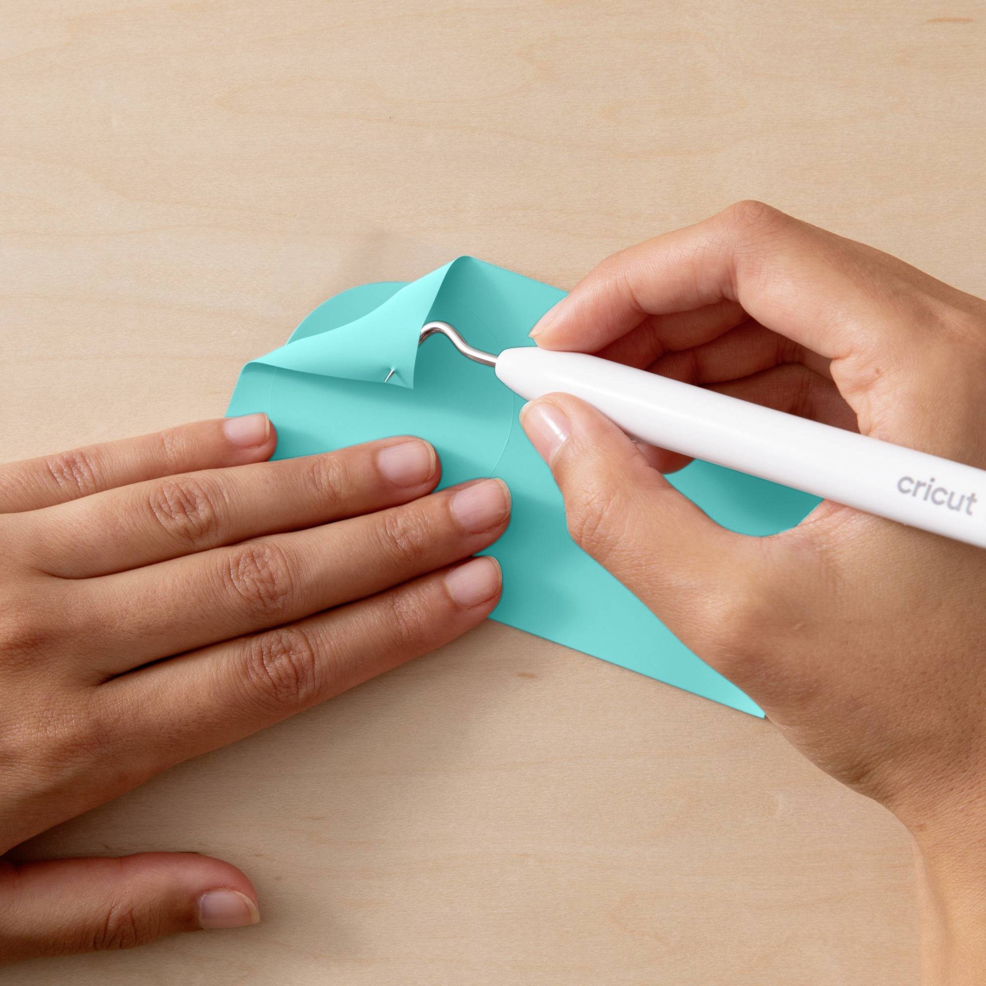 Jedna ręka używa narzędzia Cricut do odklejenia niebieskiego winylu od powierzchni, podczas gdy druga ręka przytrzymuje winyl.
