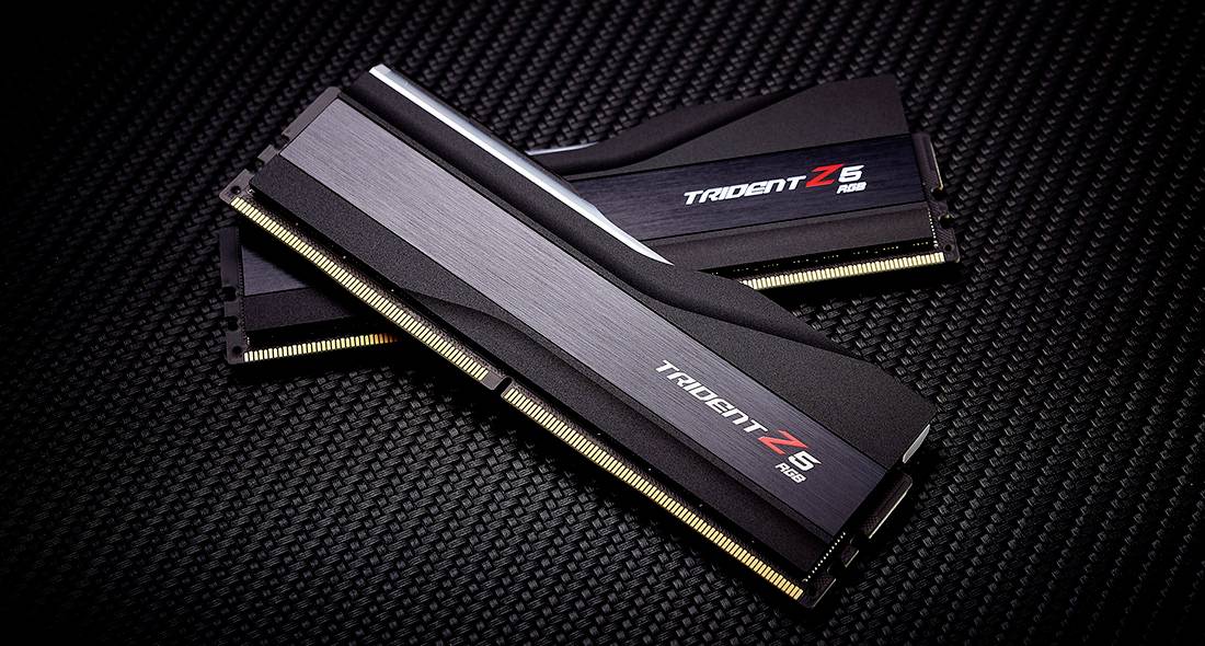 Dwa moduły RAM marki 'Trident Z5' z czarnym radiatorem, ułożone na powierzchni z włókna węglowego.