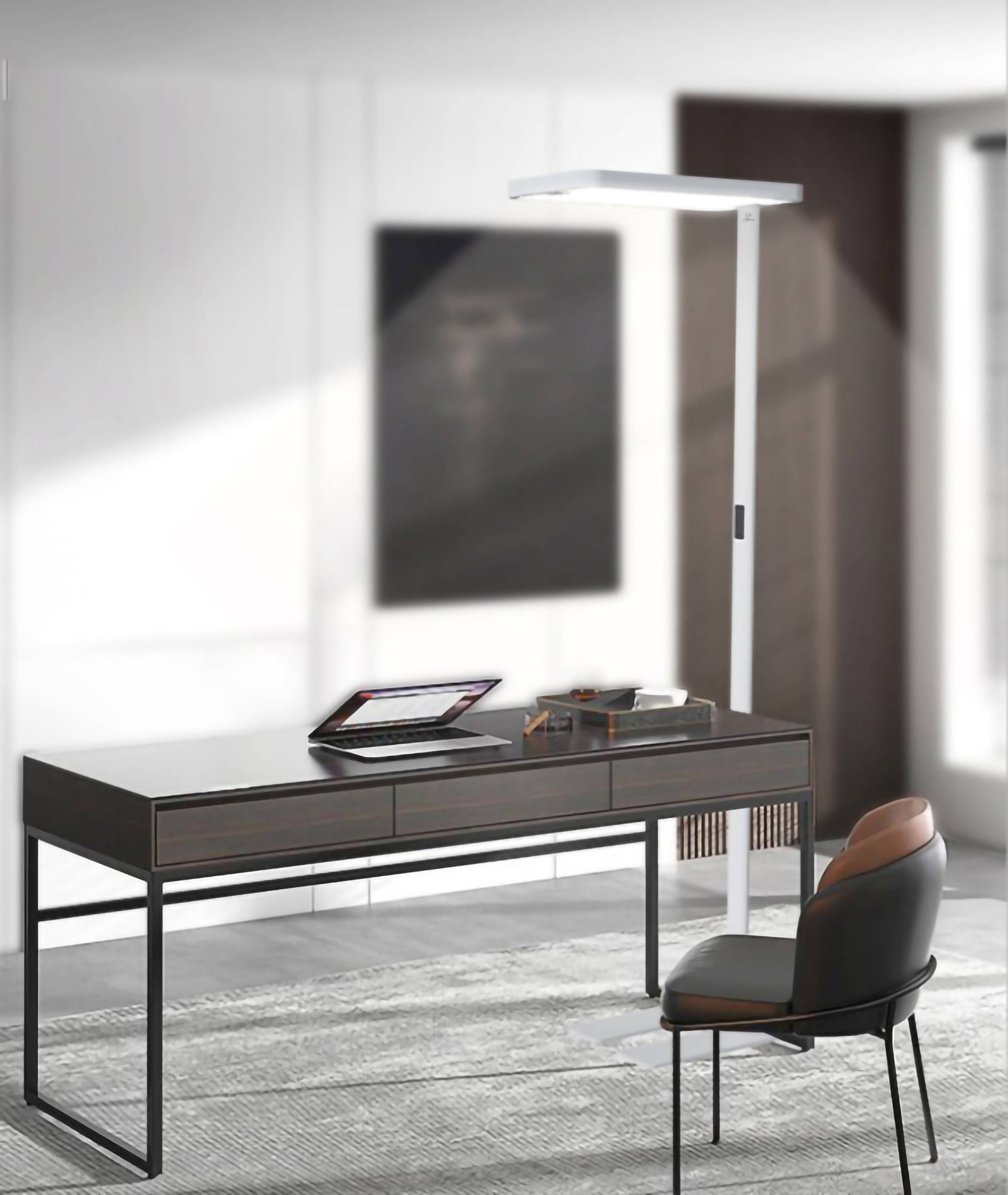 Nowoczesna, minimalistycznie urządzona przestrzeń robocza z ciemnym biurkiem, na którym znajduje się laptop i artykuły biurowe, obok stoi tapicerowany fotel.