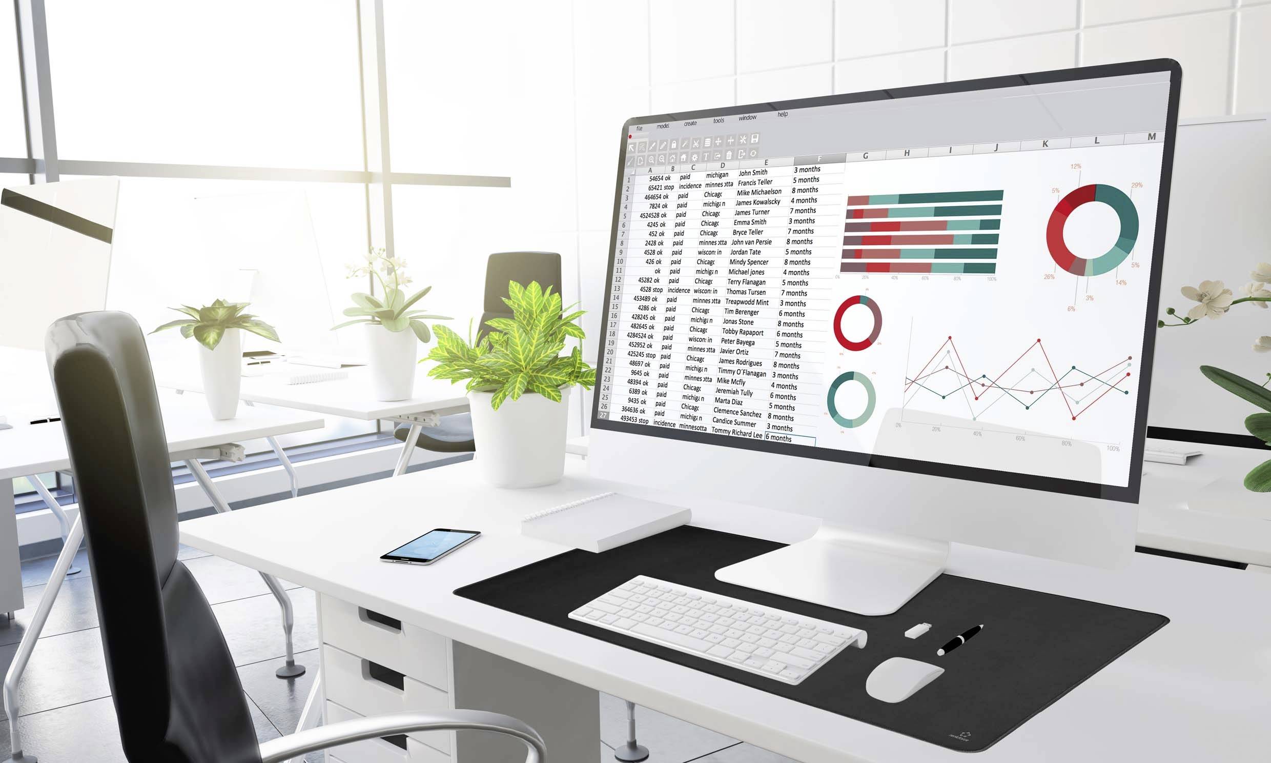 Nowoczesna, jasna przestrzeń biurowa z dużym monitorem wyświetlającym tabele i wykresy danych sprzedażowych. Na biurku stoją rośliny.