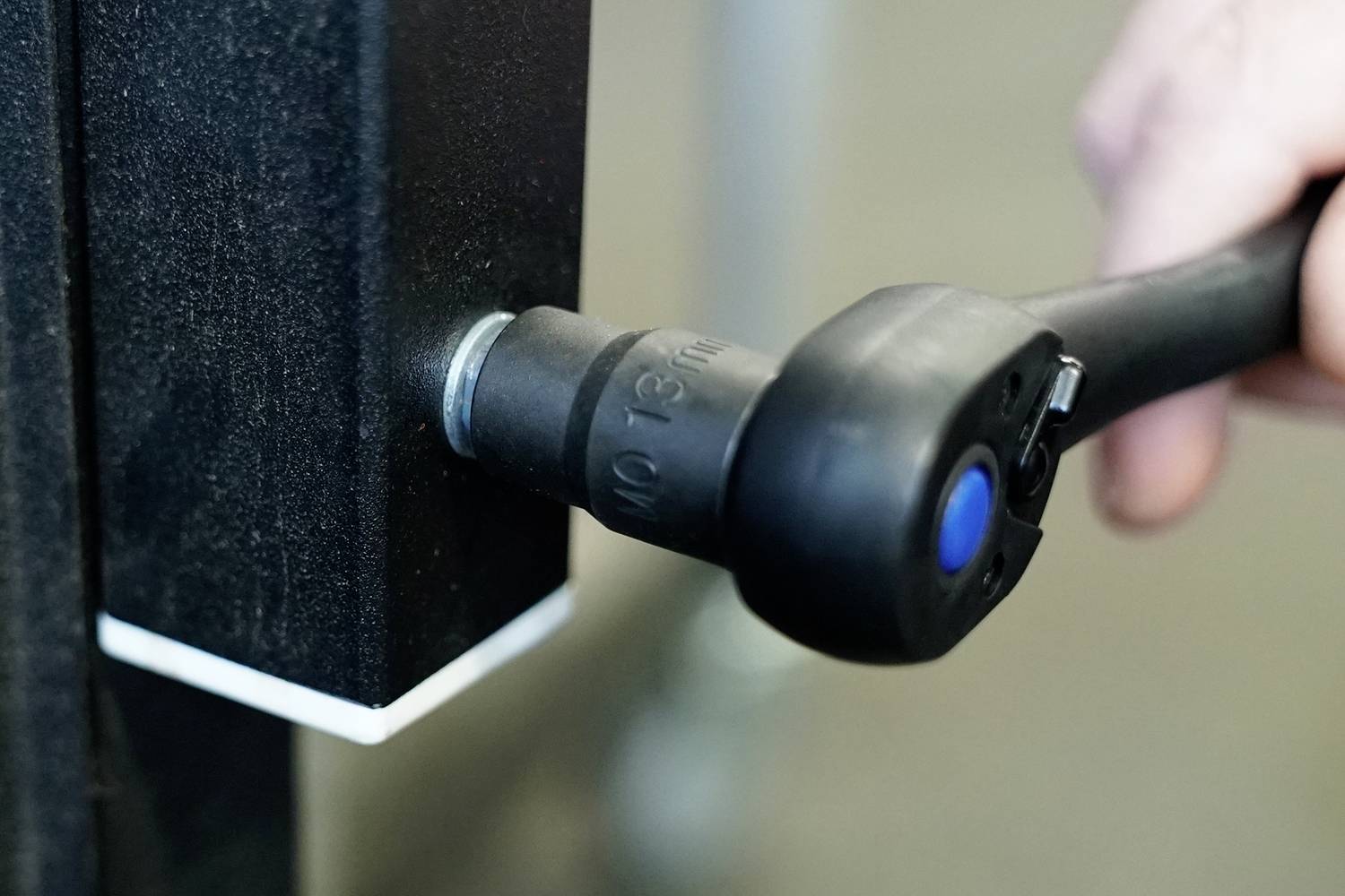 Ręka dokręca czarną nakrętkę kluczem do nakrętek, zamocowaną na czarnej metalowej ramie.