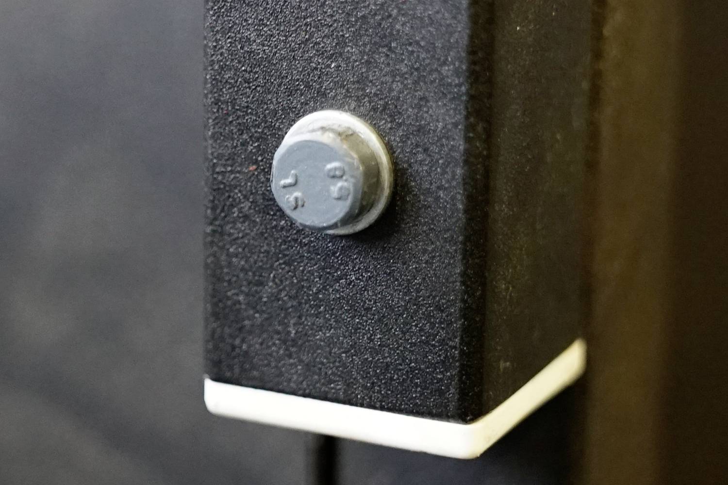 Zbliżenie czarnego metalowego słupa z wystającą szarą nakrętką. Biały pasek otacza dolną część.