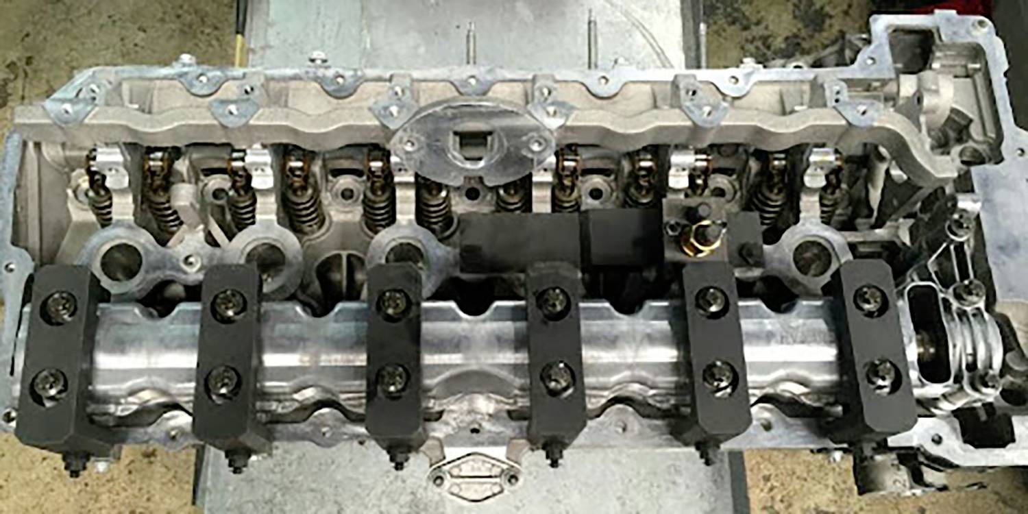 Zbliżenie otwartego silnika samochodowego, ukazujące zawory, wałek rozrządu i cylindry. Silnik leży na stole warsztatowym.