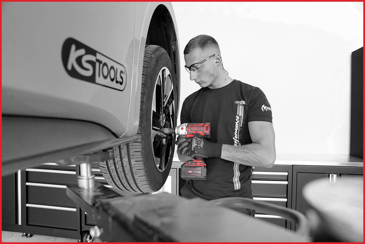 Mechanik w ochronnych okularach wymienia oponę samochodu elektrycznym kluczem dynamometrycznym w warsztacie.