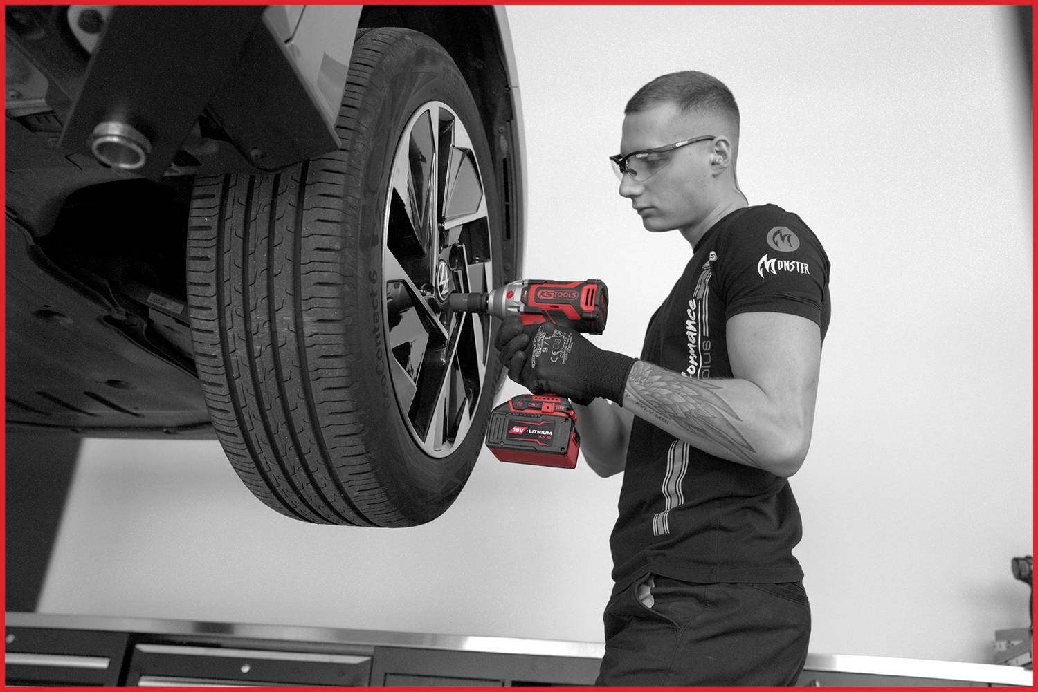 Mechanik w okularach i rękawicach dokręca nakrętkę koła w samochodzie za pomocą akumulatorowego klucza udarowego.