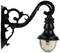 Czarna, ozdobna lampa ścienna metalowa z przezroczystym, szklanym kloszem, zamocowana na zakrzywionej podstawie.