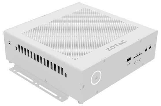 Kompaktowy biały mini komputer z otworami wentylacyjnymi, złączami USB i gniazdem słuchawkowym z przodu. Na obudowie widoczna nazwa marki 'Zotac'.