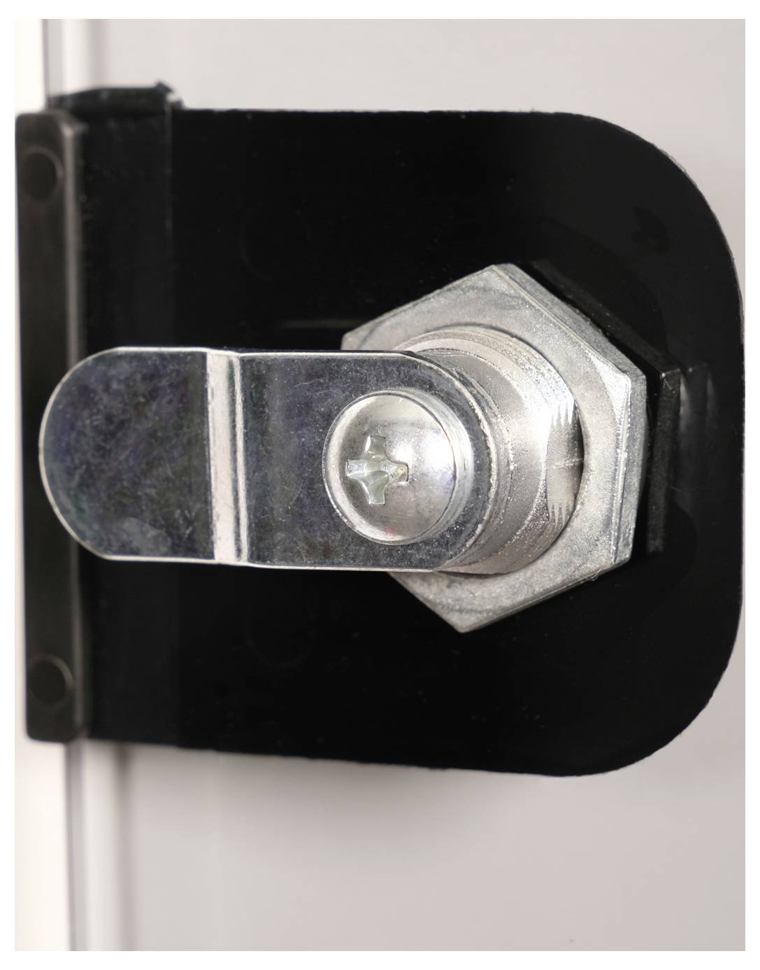 Srebrna kłódka z ryglем na czarnym uchwycie, zamocowana na białej powierzchni. Kłódka ma kształt sześciokątny.