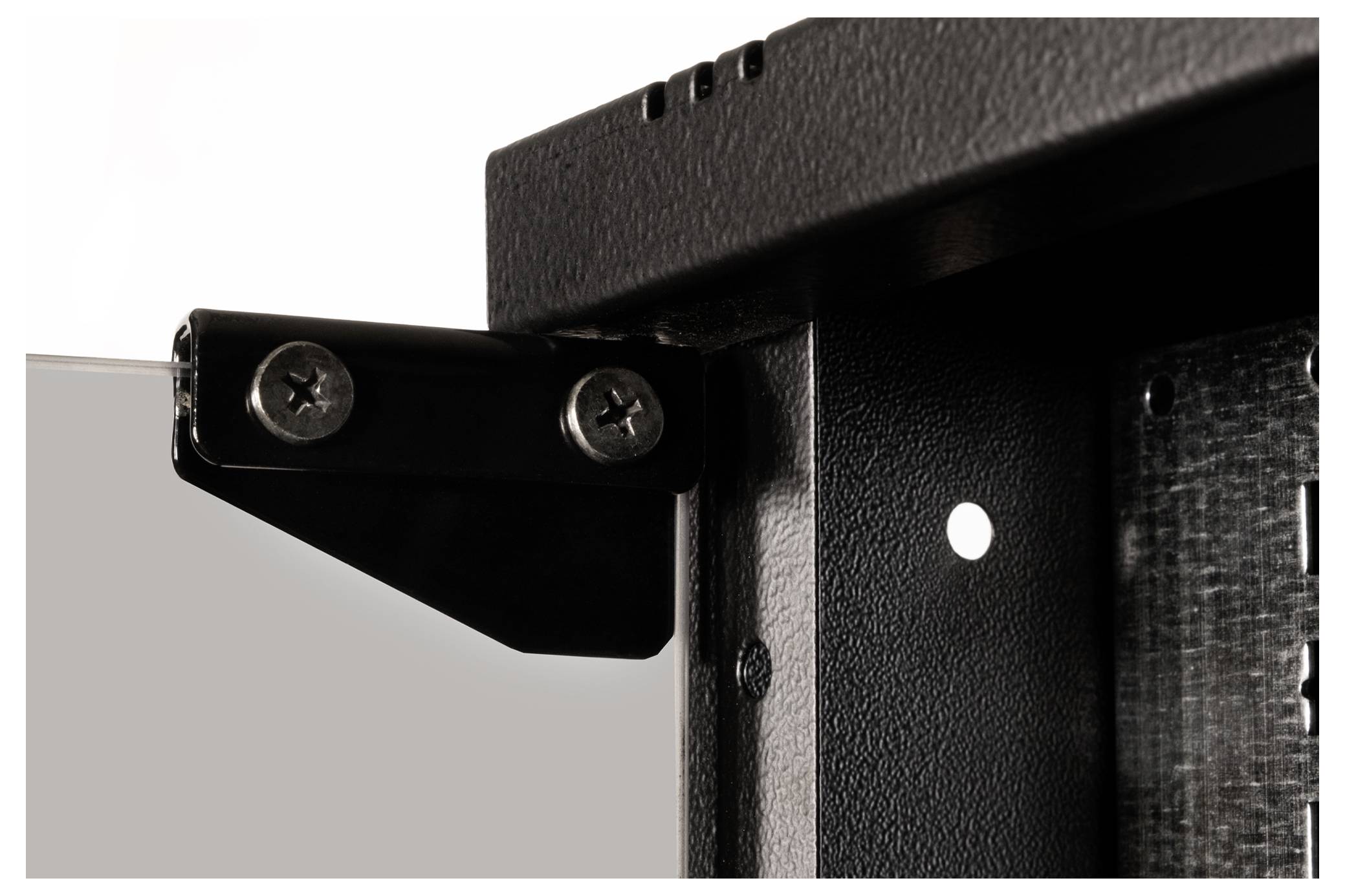 Zbliżenie czarnego zawiasu przymocowanego do metalowej ramy. Zawias jest zamontowany za pomocą dwóch srebrnych śrub.