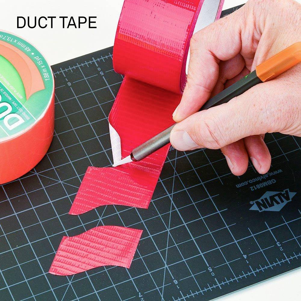 Ręka tnie czerwoną taśmę klejącą na czarnej desce do krojenia. Po lewej stronie znajduje się rolka taśmy izolacyjnej.