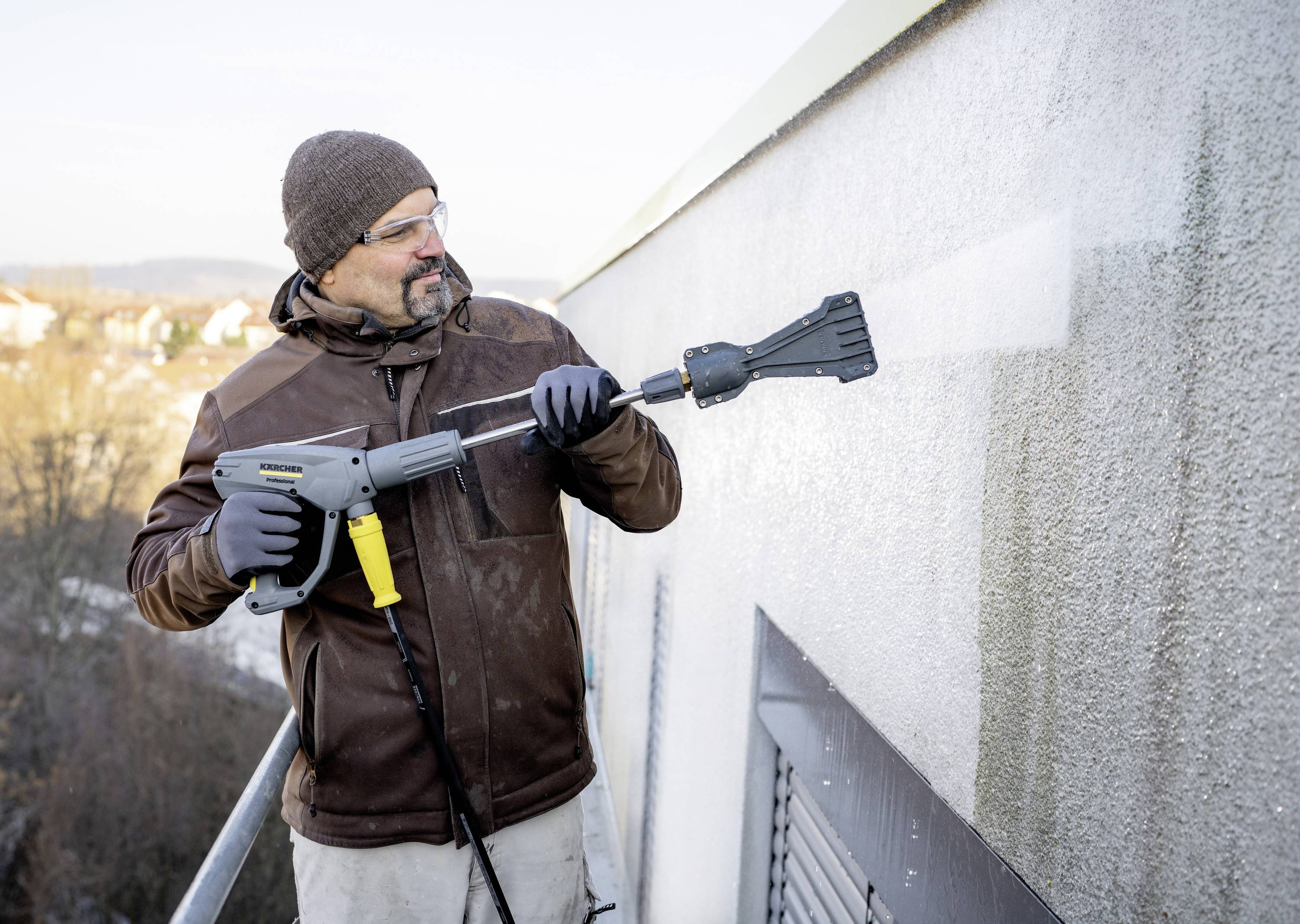 Mężczyzna czyści zewnętrzną ścianę budynku za pomocą myjki ciśnieniowej.