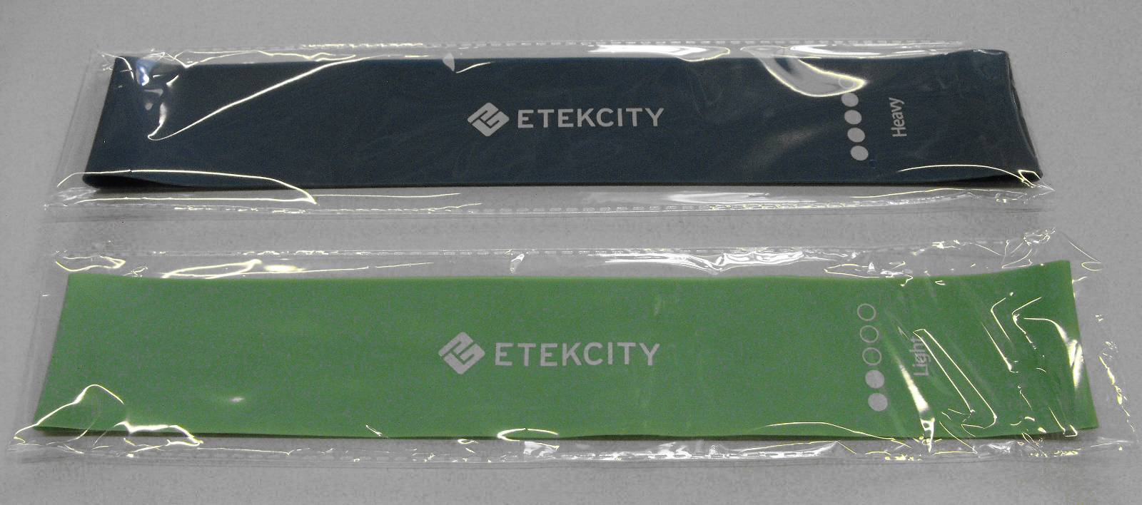 Dwie taśmy treningowe, jedna czarna, druga zielona, z logo 'ETEKCITY'. Obie taśmy są zapakowane w przezroczysty plastik.