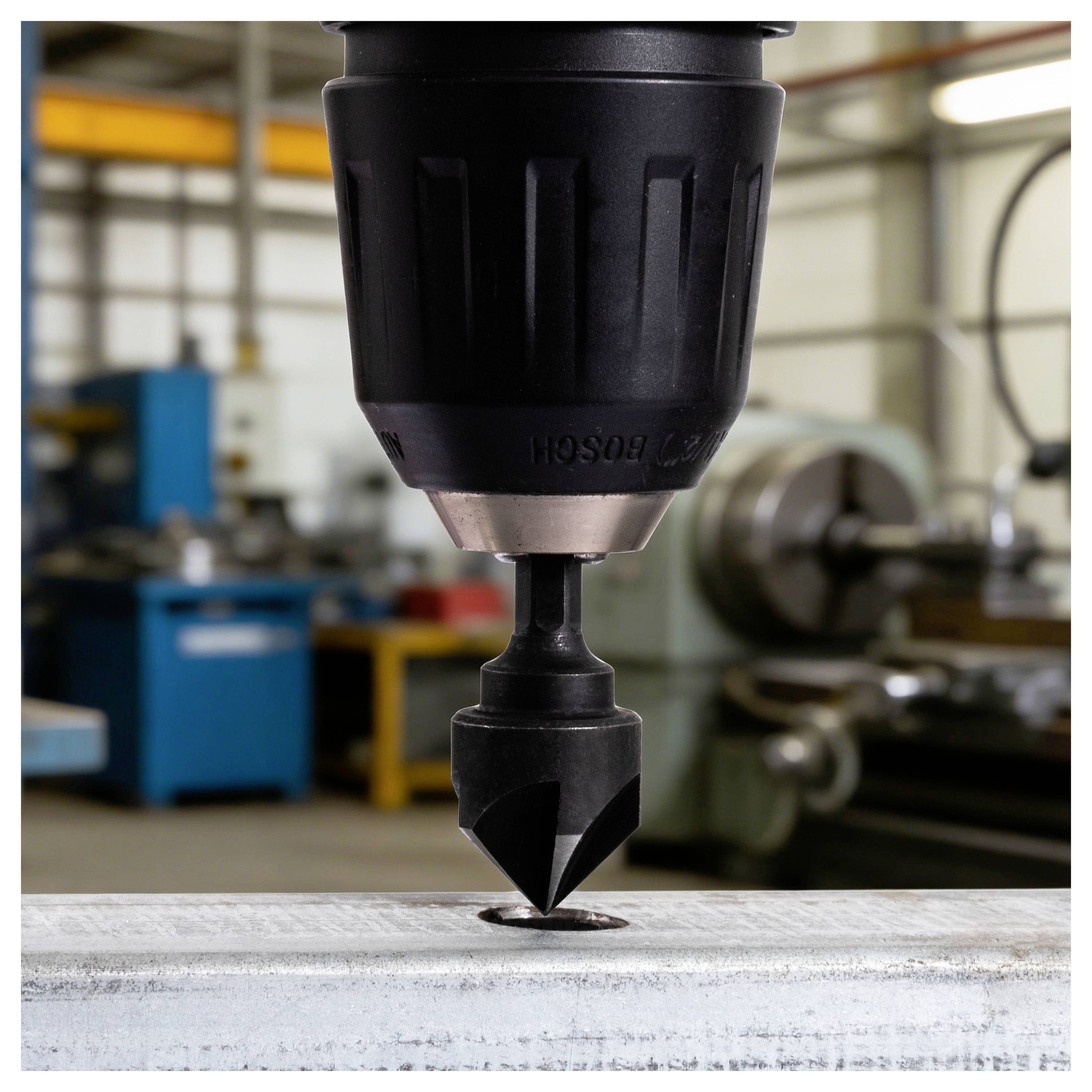 Zbliżenie wiertła maszyny wiertarskiej wcinającego się w metalową część roboczą w warsztacie.