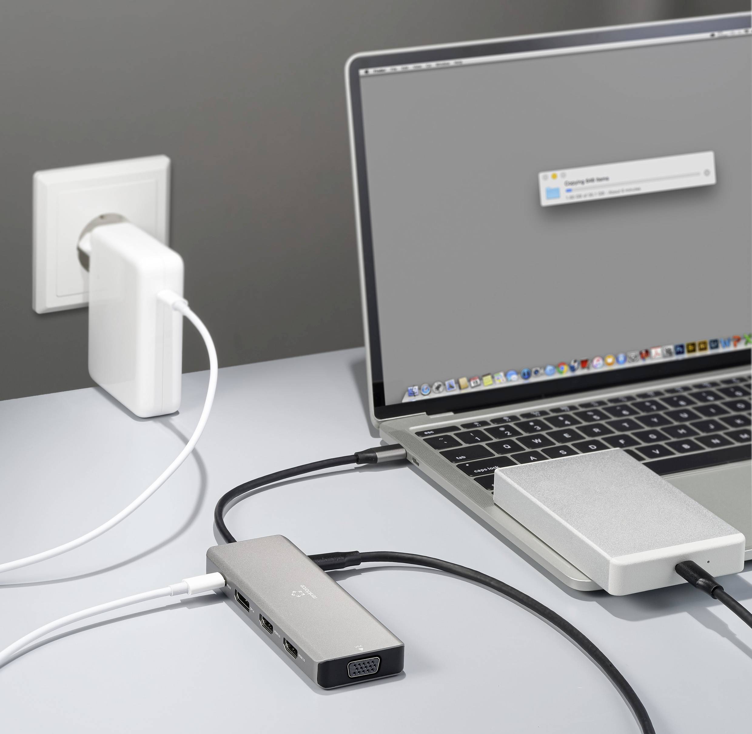 Laptop jest podłączony do gniazdka elektrycznego za pomocą kilku kabli i adapterów. Na ekranie pojawia się szare okno.