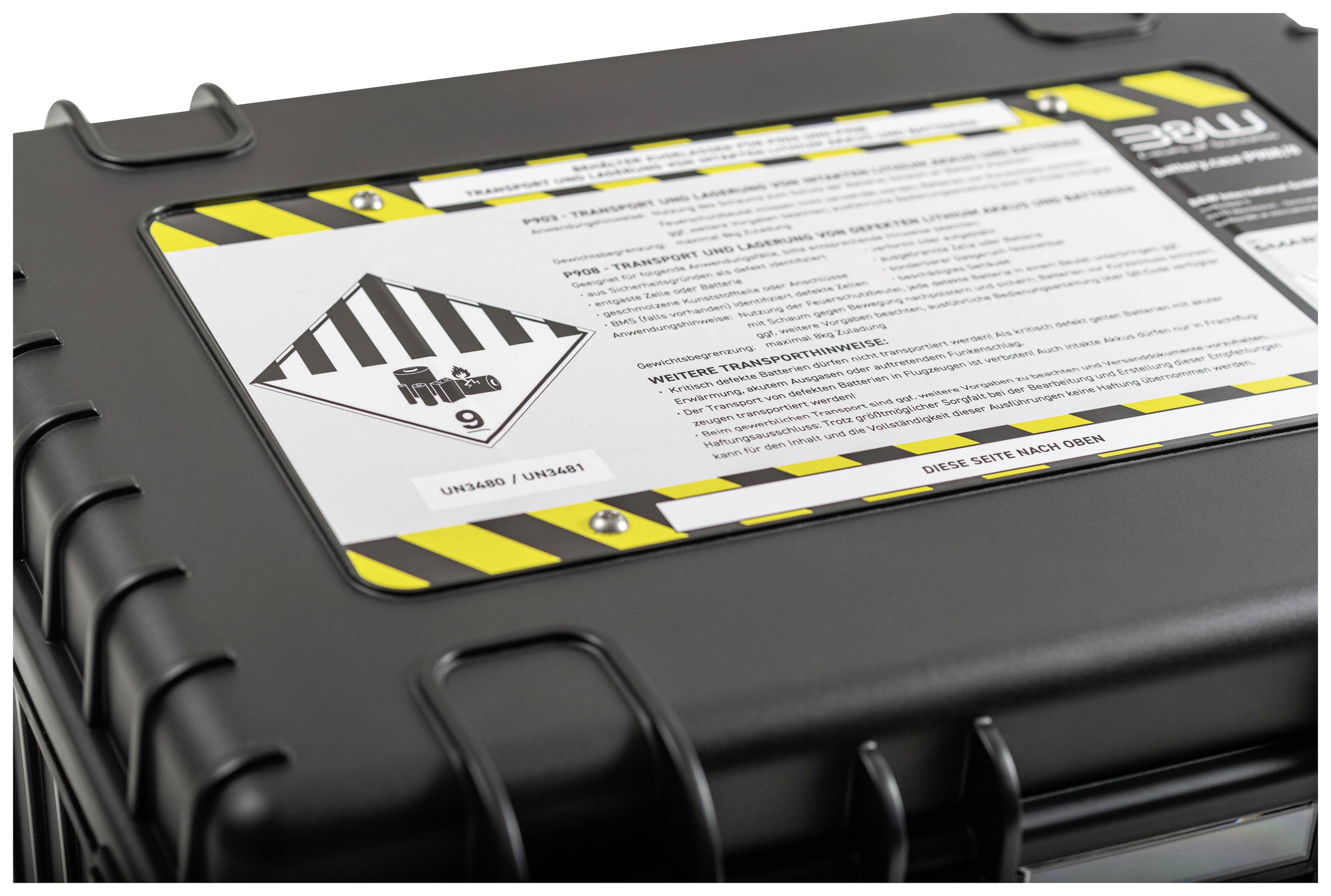 Czarny kontener transportowy z żółto-czarnym oznakowaniem ostrzegawczym oraz etykietą materiałów niebezpiecznych klasy 9. Wierzchnia strona zawiera instrukcję bezpieczeństwa.