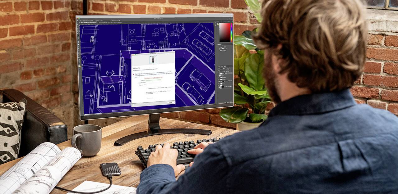 Mężczyzna pracuje przy komputerze, korzystając z programu architektonicznego. Na ekranie widoczny jest plan budowlany i wyskakujące okno. Na biurku leży linijka.