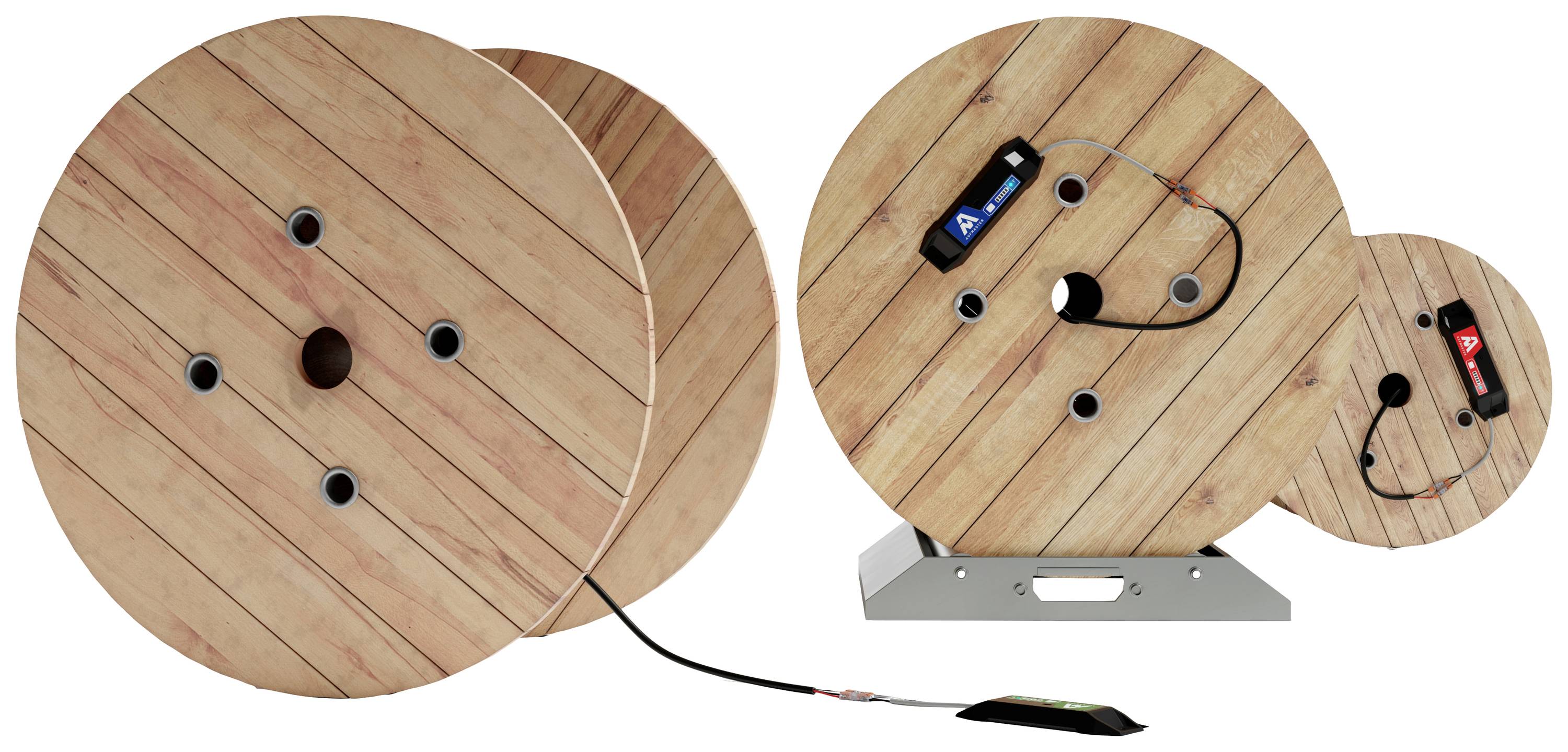 Trzy duże, puste drewniane bębny kablowe. Jeden z nich posiada panel słoneczny i kable, które kończą się podłączonym akumulatorem z niebieskim wyświetlaczem.